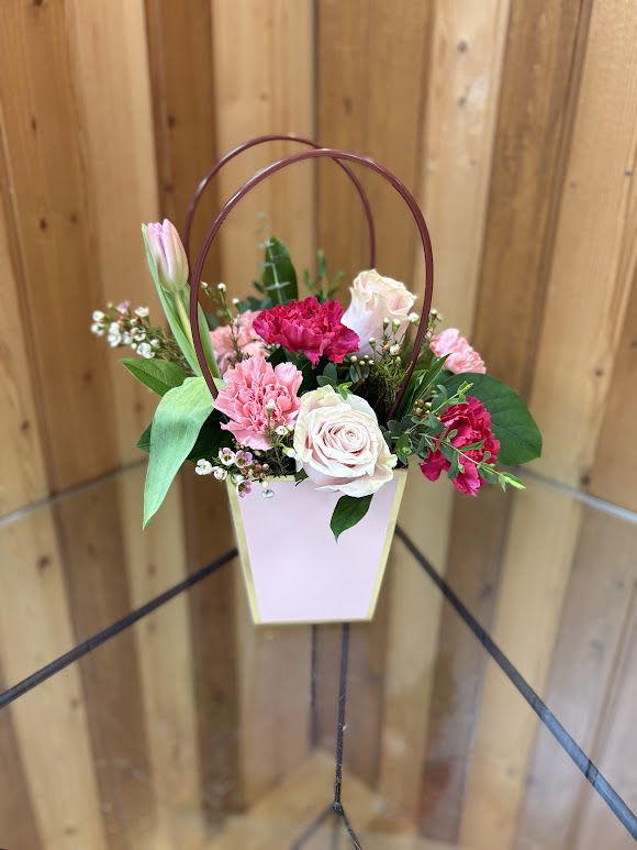 Purse-onally Yours - A soft, handbag-style arrangement that reads like a love note in flowers - perfect as an anniversary, birthday, Valentine's Day, Mother's Day, or just-because gift. Purse-onally Yours pairs pale pink roses, deeper pink carnations, and a single light-pink tulip that rises above the bouquet to create a romantic focal point; delicate white accents and lush greenery fill the composition for a full, feminine look that feels cheerful and intimate. Presented in a tall, tapered pink box vase with gold trim and two slim arched handles, the design echoes a petite purse and makes a memorable presentation that will make her feel truly seen.  Measuring to fit your tabletop or bedside, this arrangement blends long-lasting carnations and roses with seasonal tulip bloom for a textural mix of ruffled and velvety petals. The pink box vase doubles as a keepsake; handle detail gives the piece a basket-like silhouette ideal for summer parties, retirements, thank-you gifts, Women's Day, Best Friends Day, or romantic moments. Substitutions may be necessary based on seasonal availability, but we'll always match the color palette and overall style you see here.  Haehn Florist, Greenhouses, &amp; Flower Delivery - 410 Hamilton Rd. Wapakoneta. Find us on Facebook: www.facebook.com/haehnflorist
