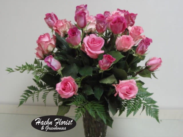 Pink roses arranged in a clear glass vase with fern accents.