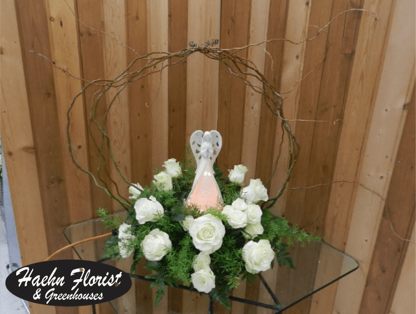 White roses arranged around a small angel figurine in a circular twig frame