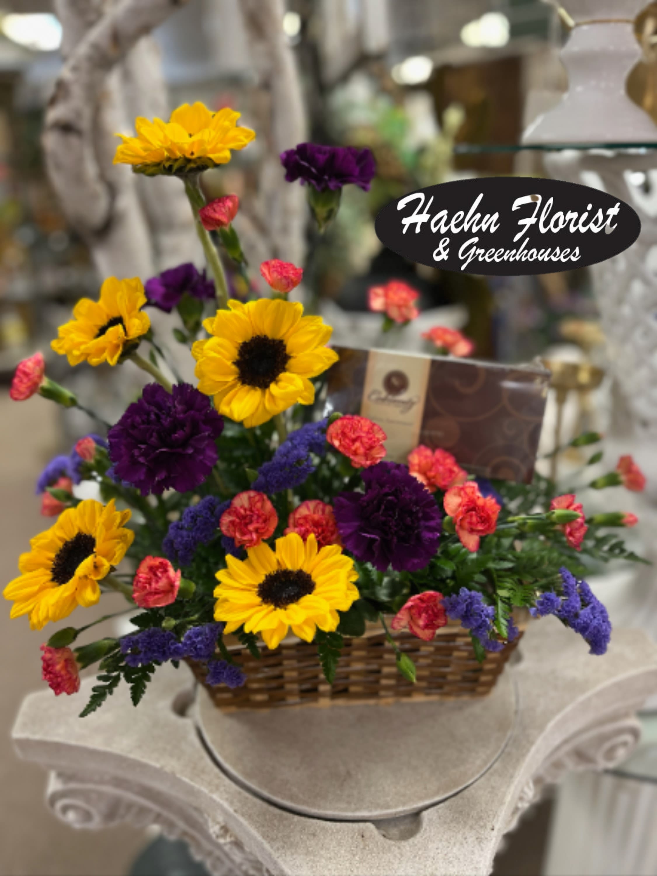Basket arrangement with yellow sunflowers, purple carnations, and pink spray carnations