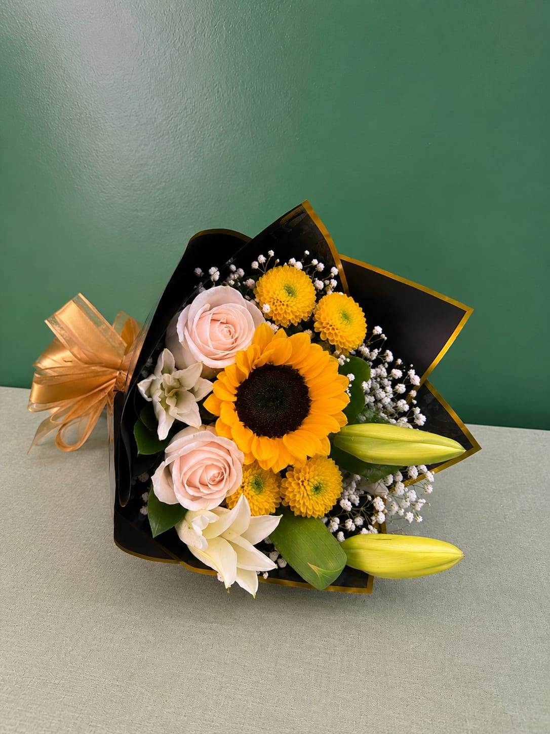 Bouquet of sunflowers, pale pink roses, and white lilies wrapped in black paper