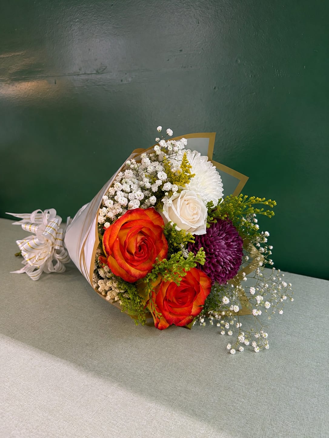 Bouquet of orange roses, white blooms, and purple flowers wrapped in paper