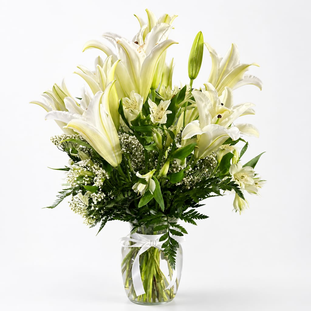 White lilies arranged in a clear glass vase with a white ribbon