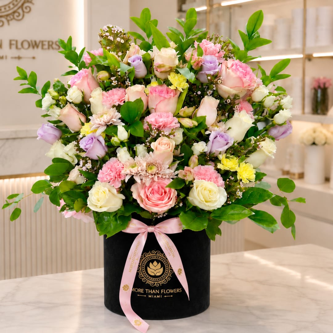 Mixed pink, white, and lavender flowers in a black hatbox with a pink ribbon