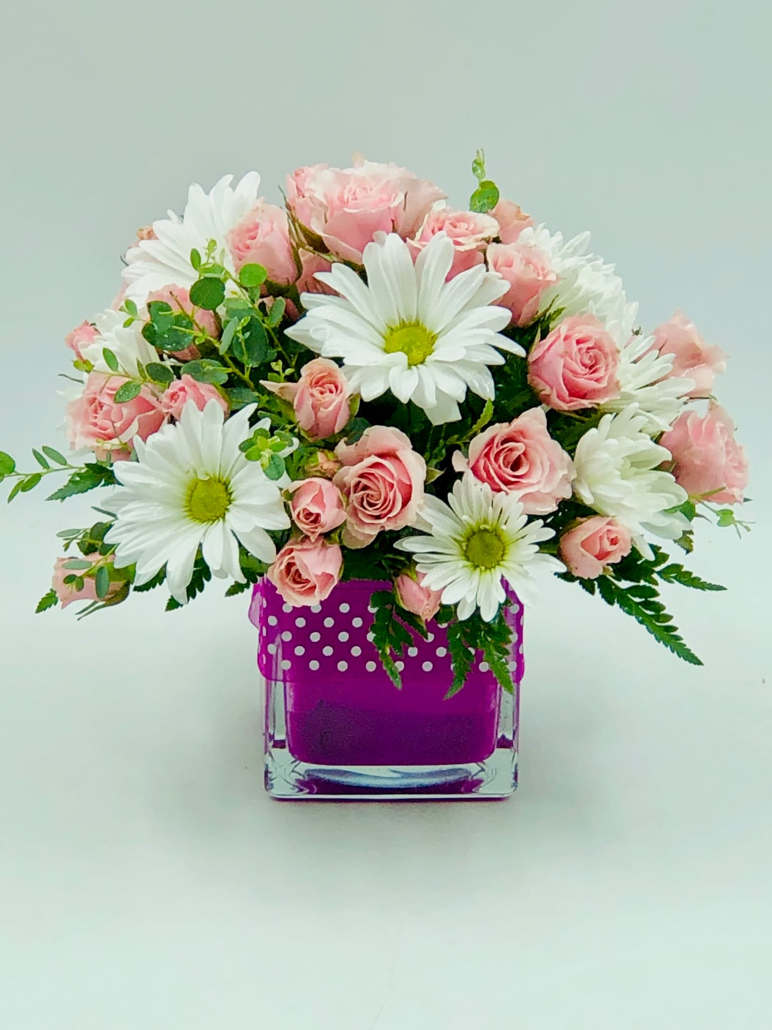 Pink roses and white daisies arranged in a purple glass vase