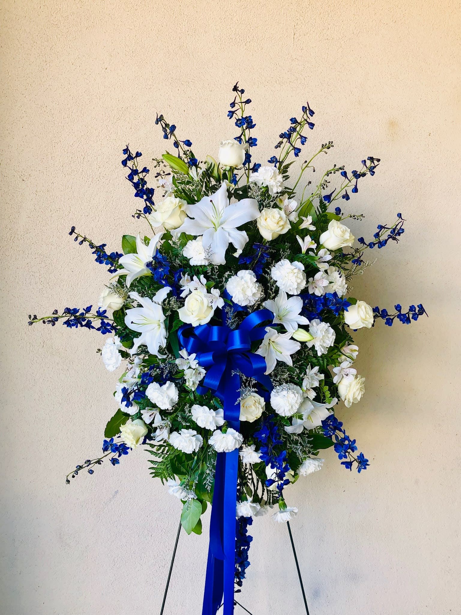 Standing floral spray of white lilies and roses with blue flowers and ribbon