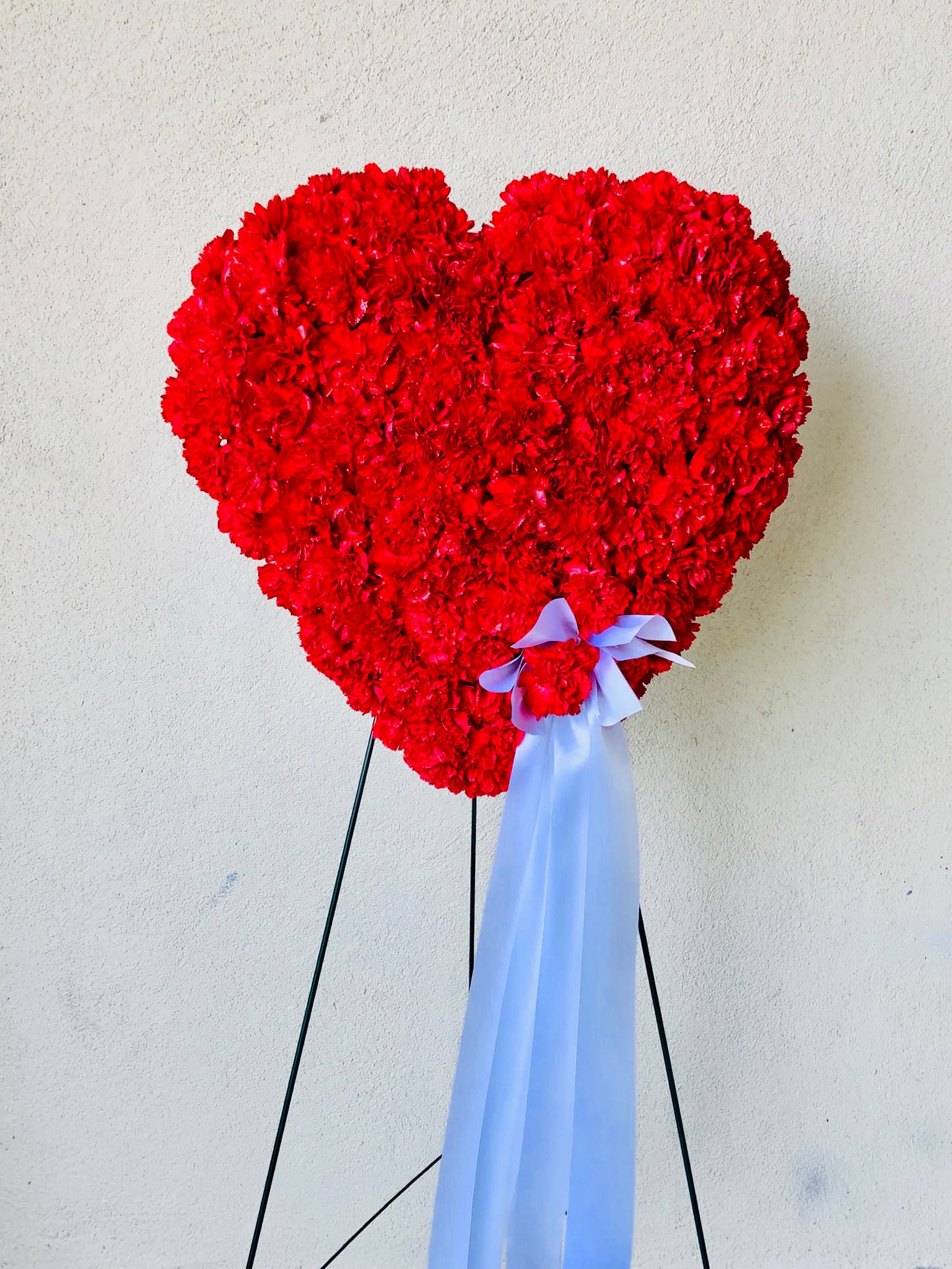 Heart-shaped red floral arrangement on a stand with a pale ribbon