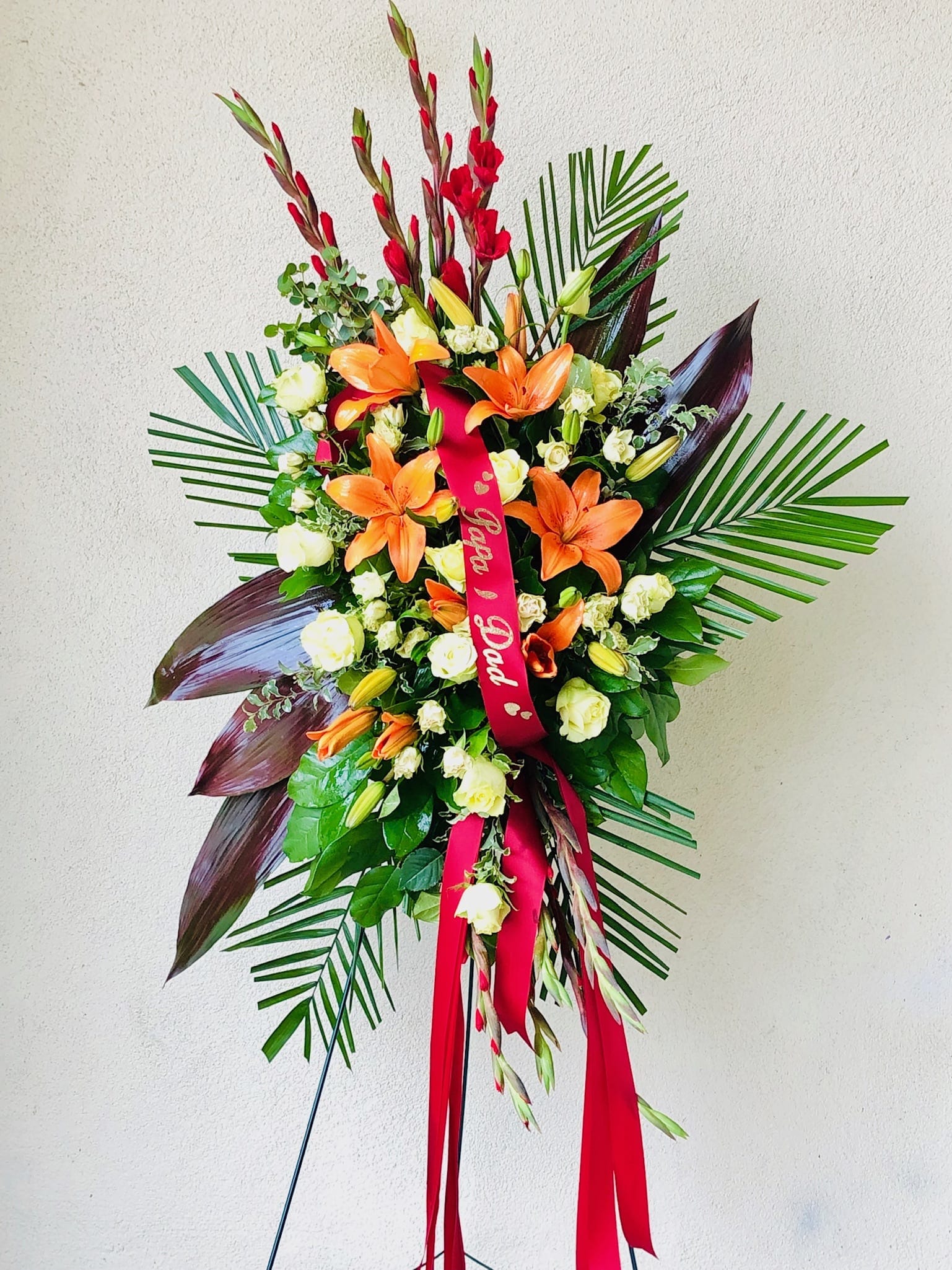 Standing floral spray with orange lilies and white roses on a red ribbon