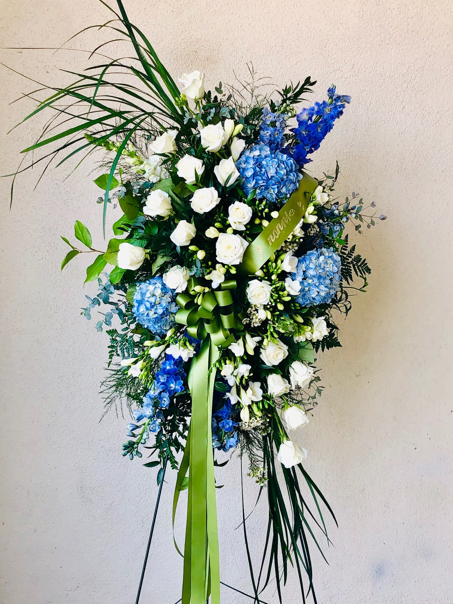 Standing floral spray with white roses and blue hydrangeas on a ribboned easel