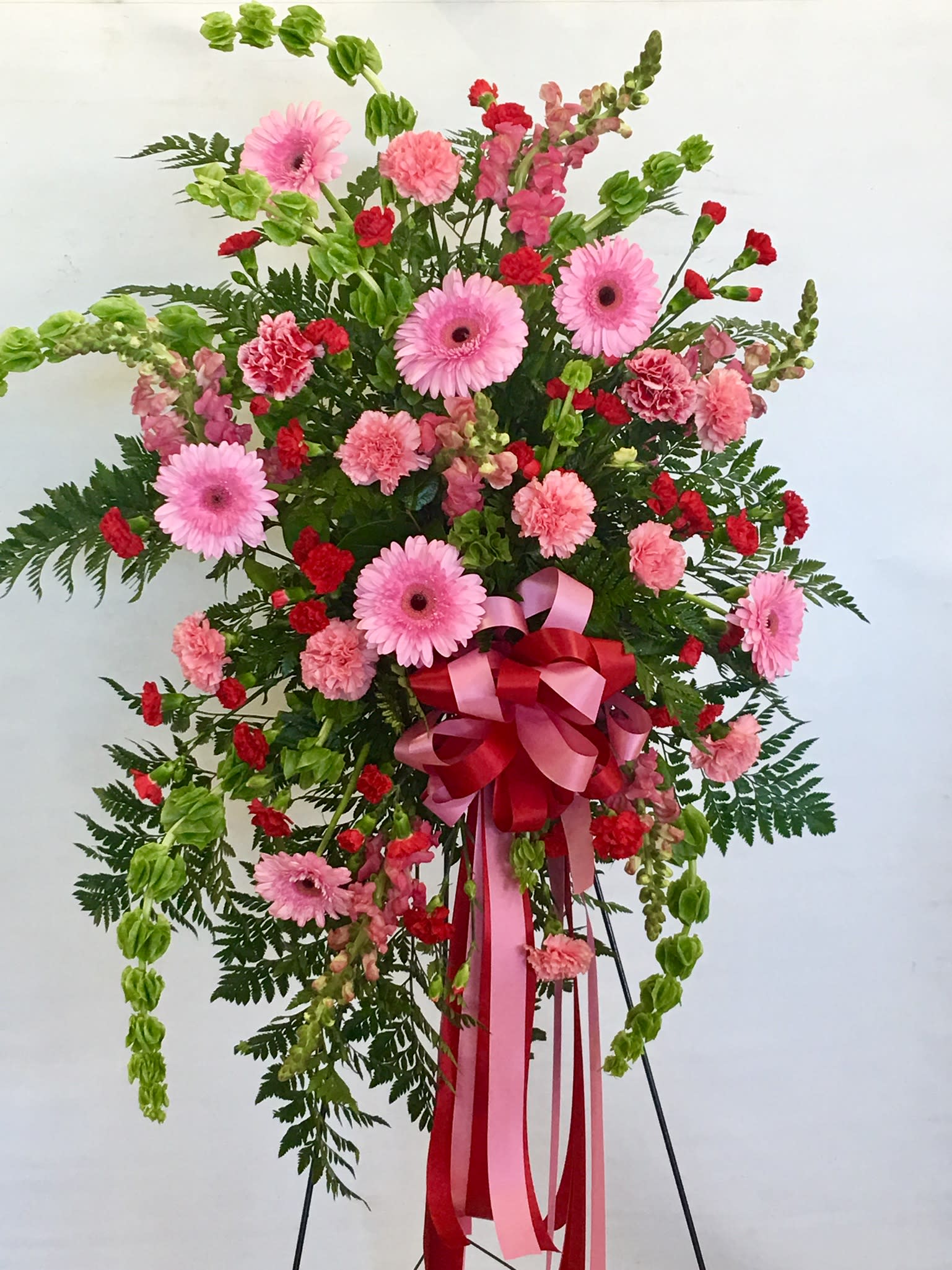Standing floral spray with pink gerberas, carnations, and red accents