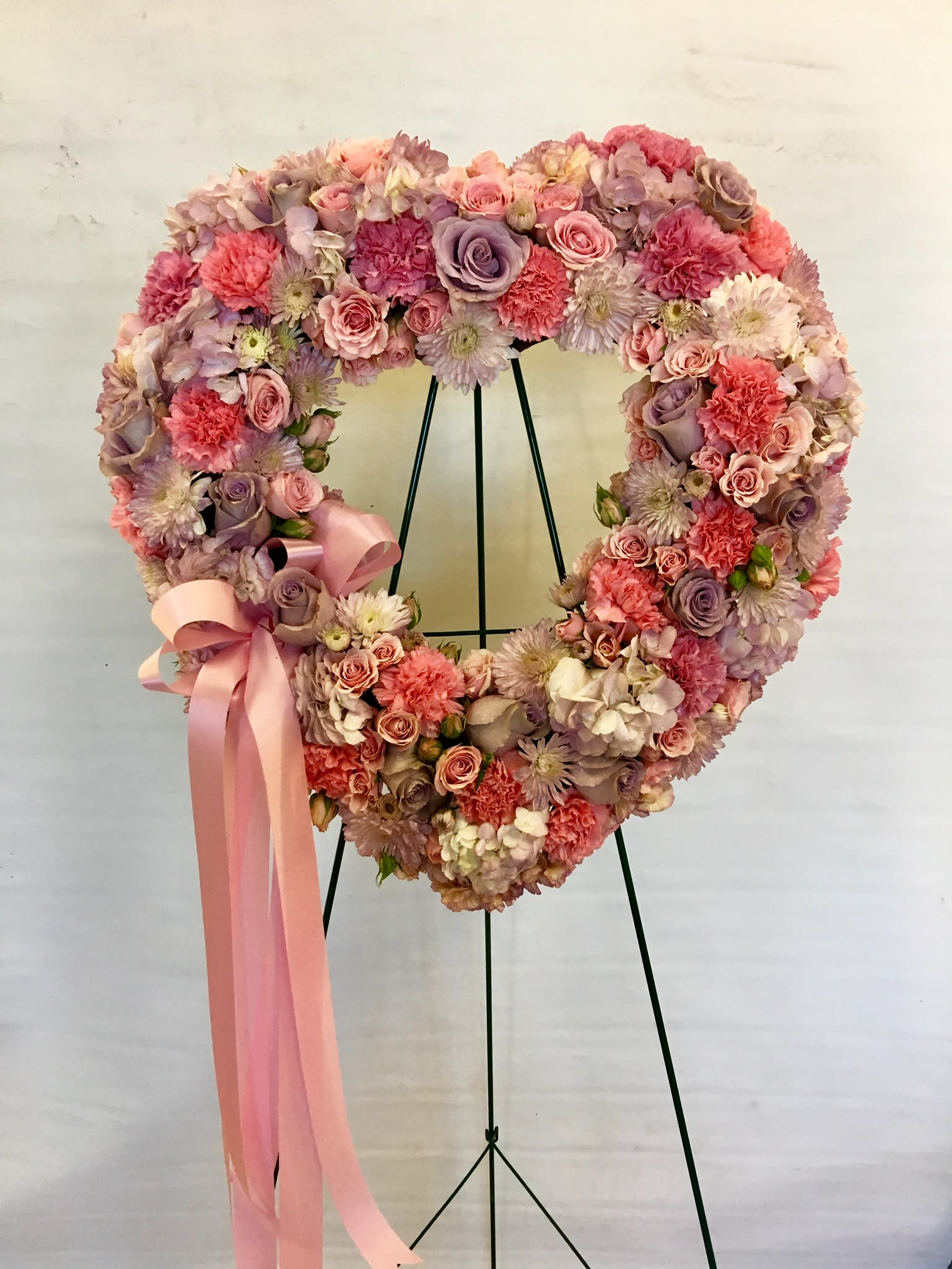 Heart-shaped floral wreath with pink and lavender blooms and a pink ribbon
