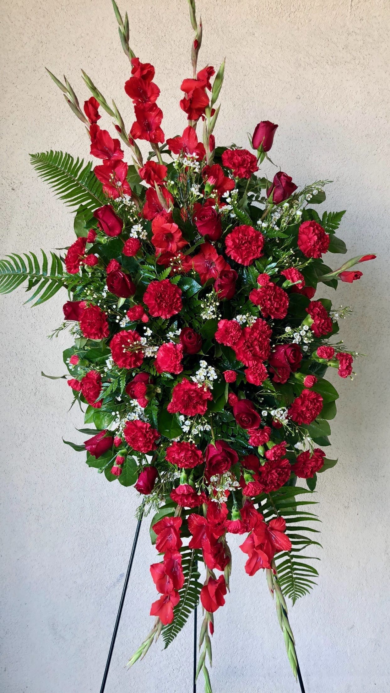Tall standing spray of red flowers with greenery on a black easel