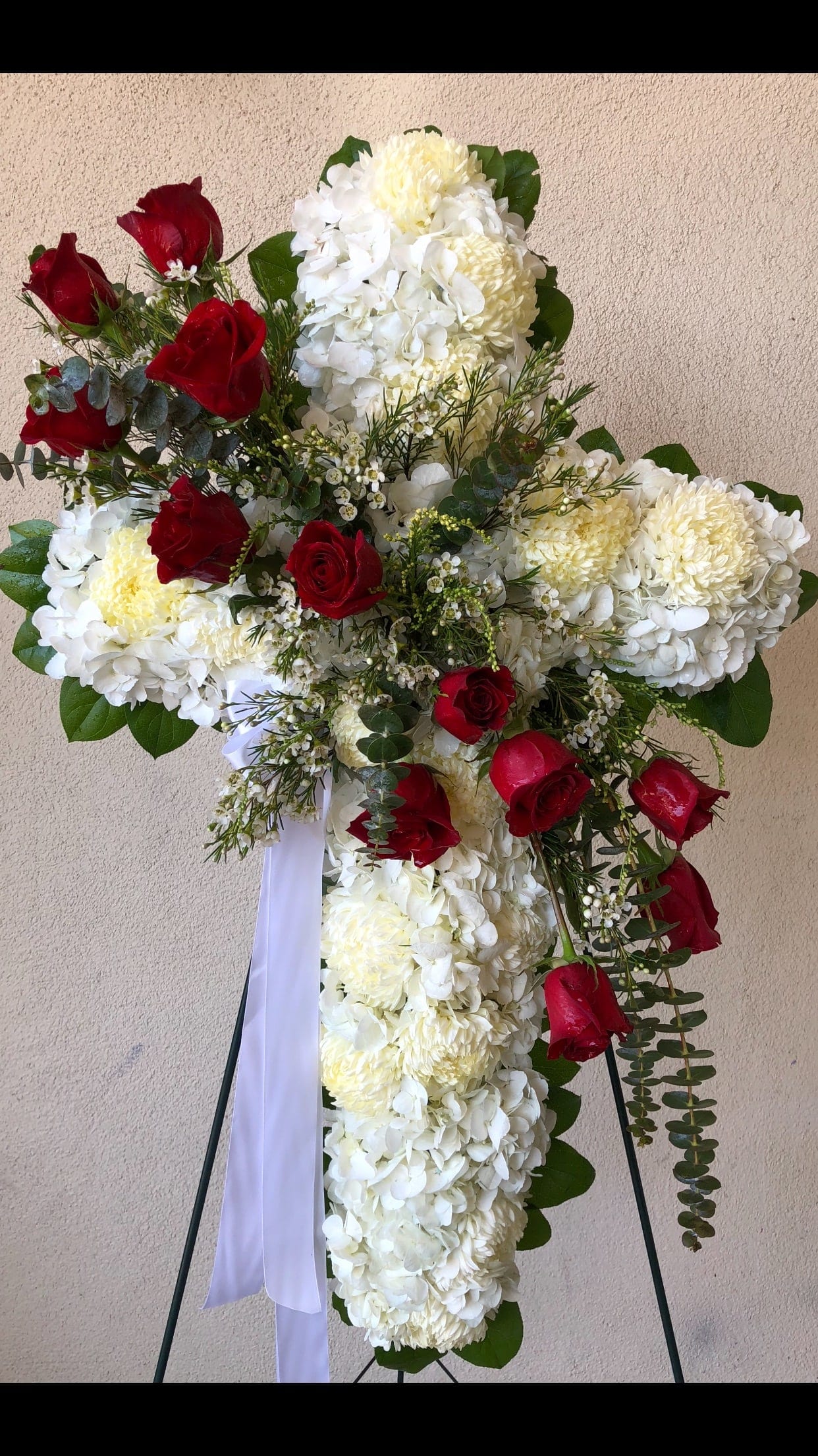Cross-shaped floral tribute with white blooms and red roses on a stand