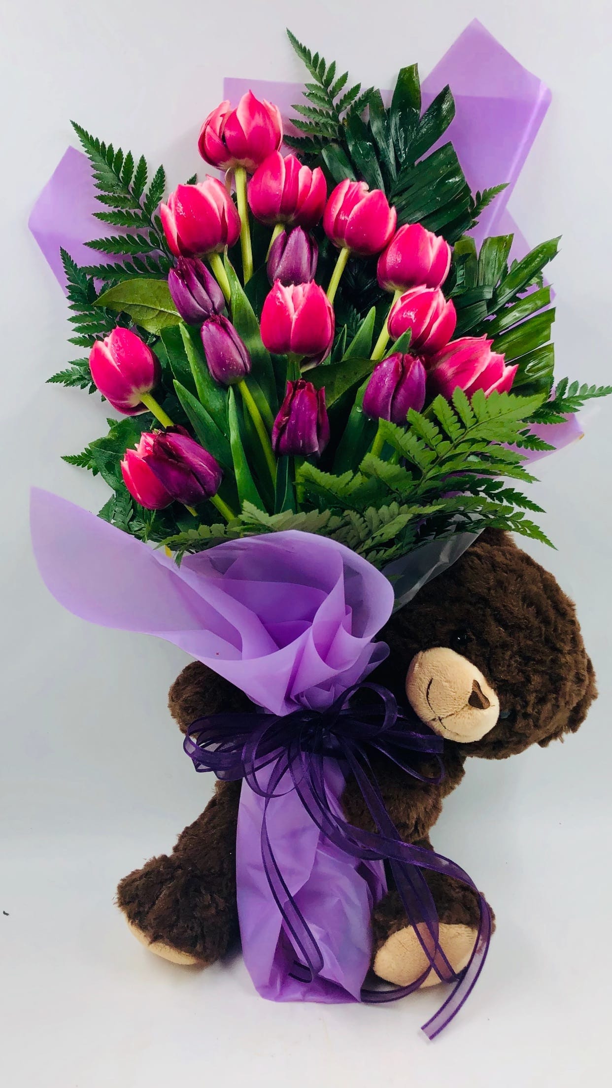 Bouquet of pink and purple tulips wrapped with purple paper, held by a teddy bear