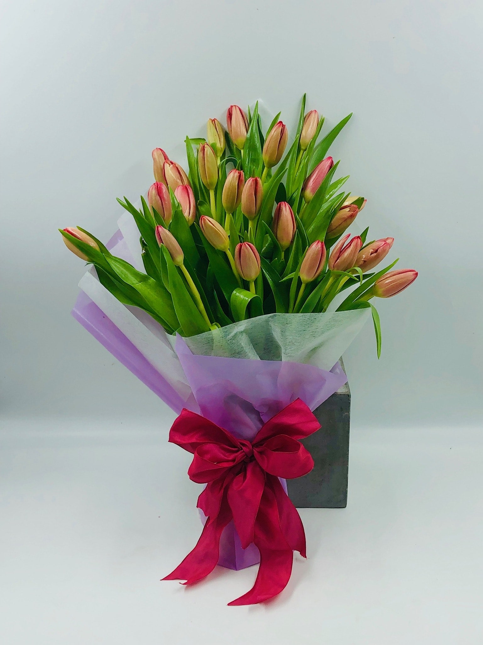 Bouquet of pink tulips wrapped in purple paper with a red ribbon