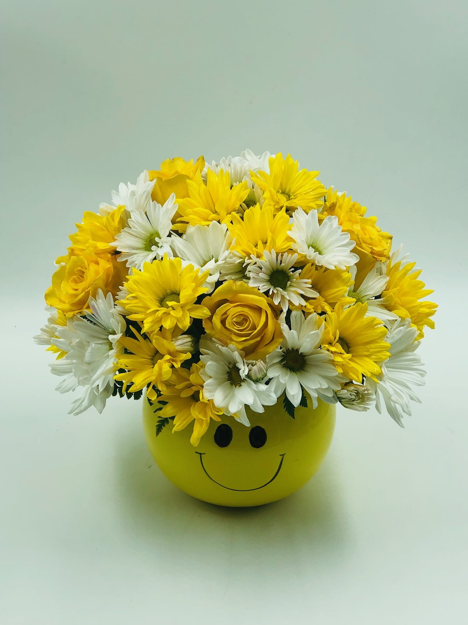 Yellow and white flowers arranged in a smiley-face pot