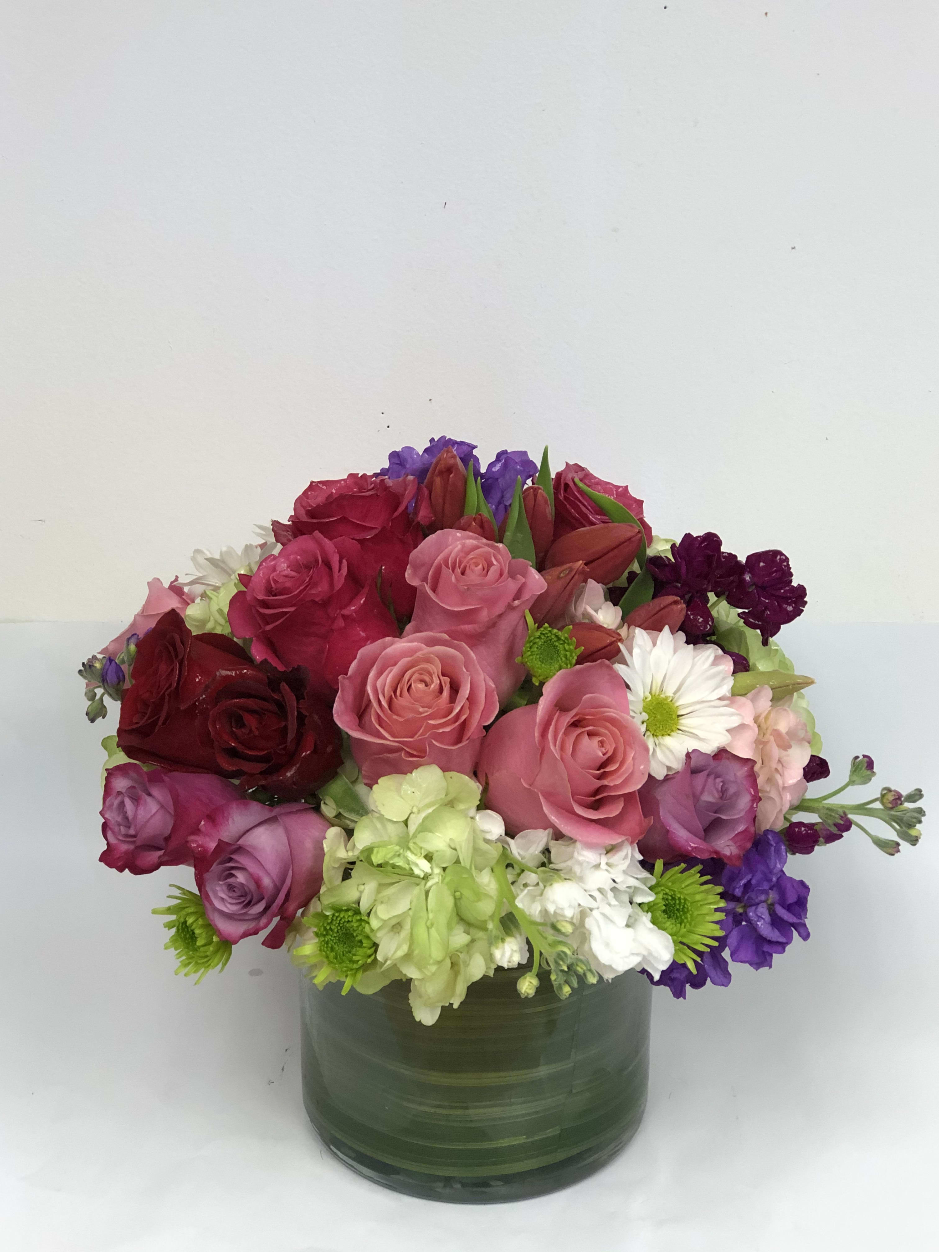 Mixed bouquet of roses, lilies, and daisies in a green glass vase