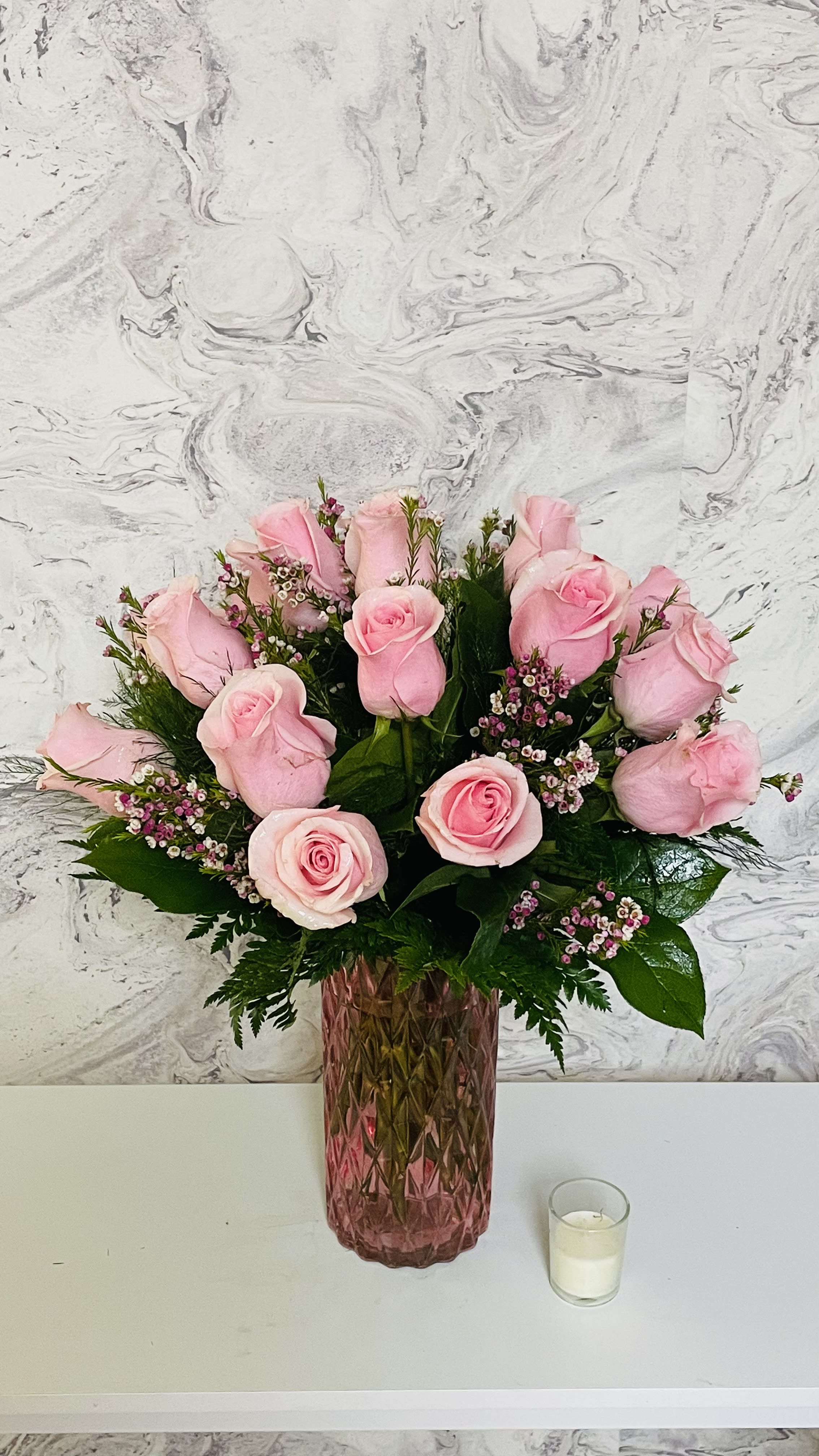 Pink roses arranged in a tall pink glass vase with a small candle nearby