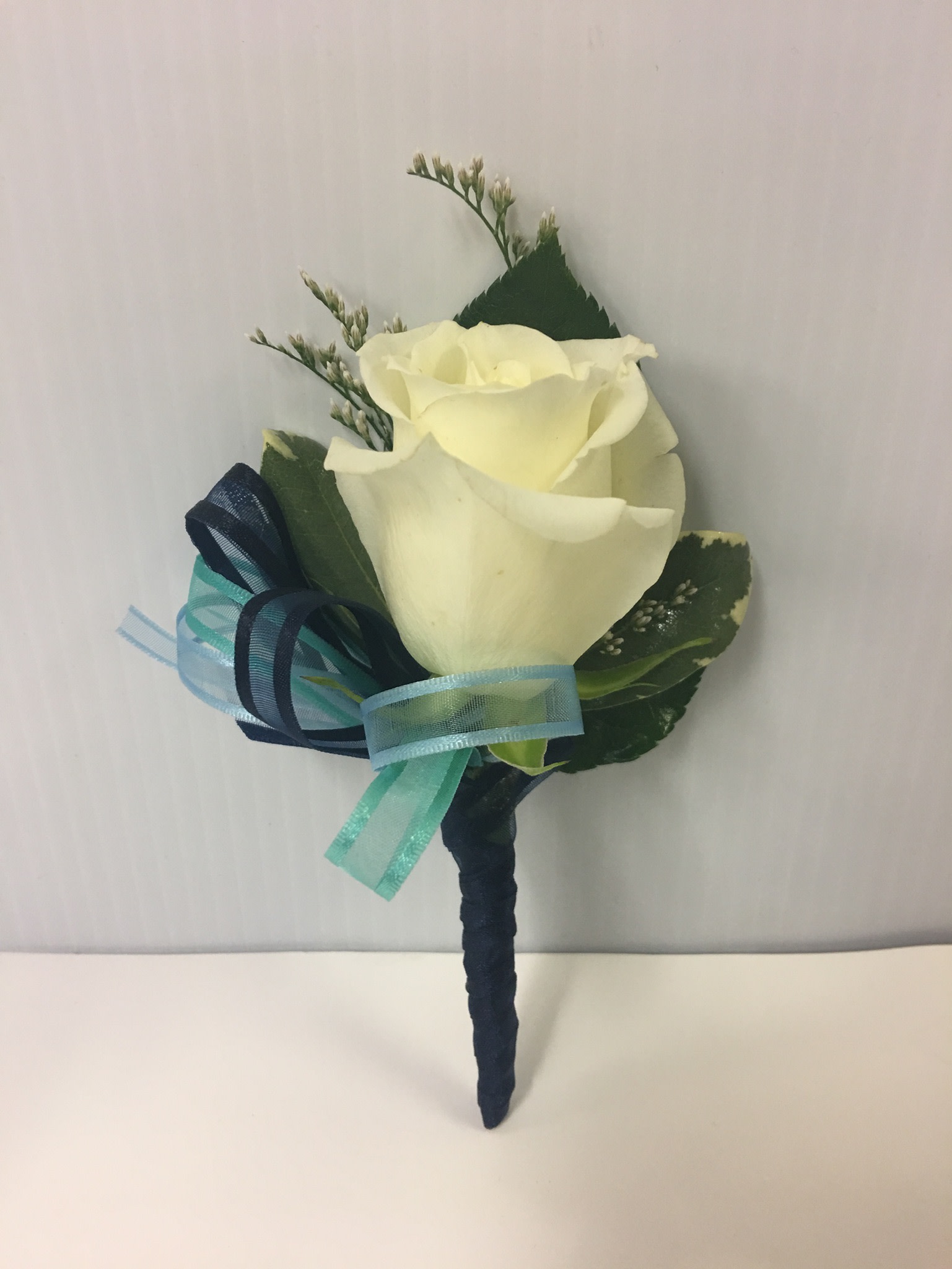 White rose boutonniere with blue ribbon accents