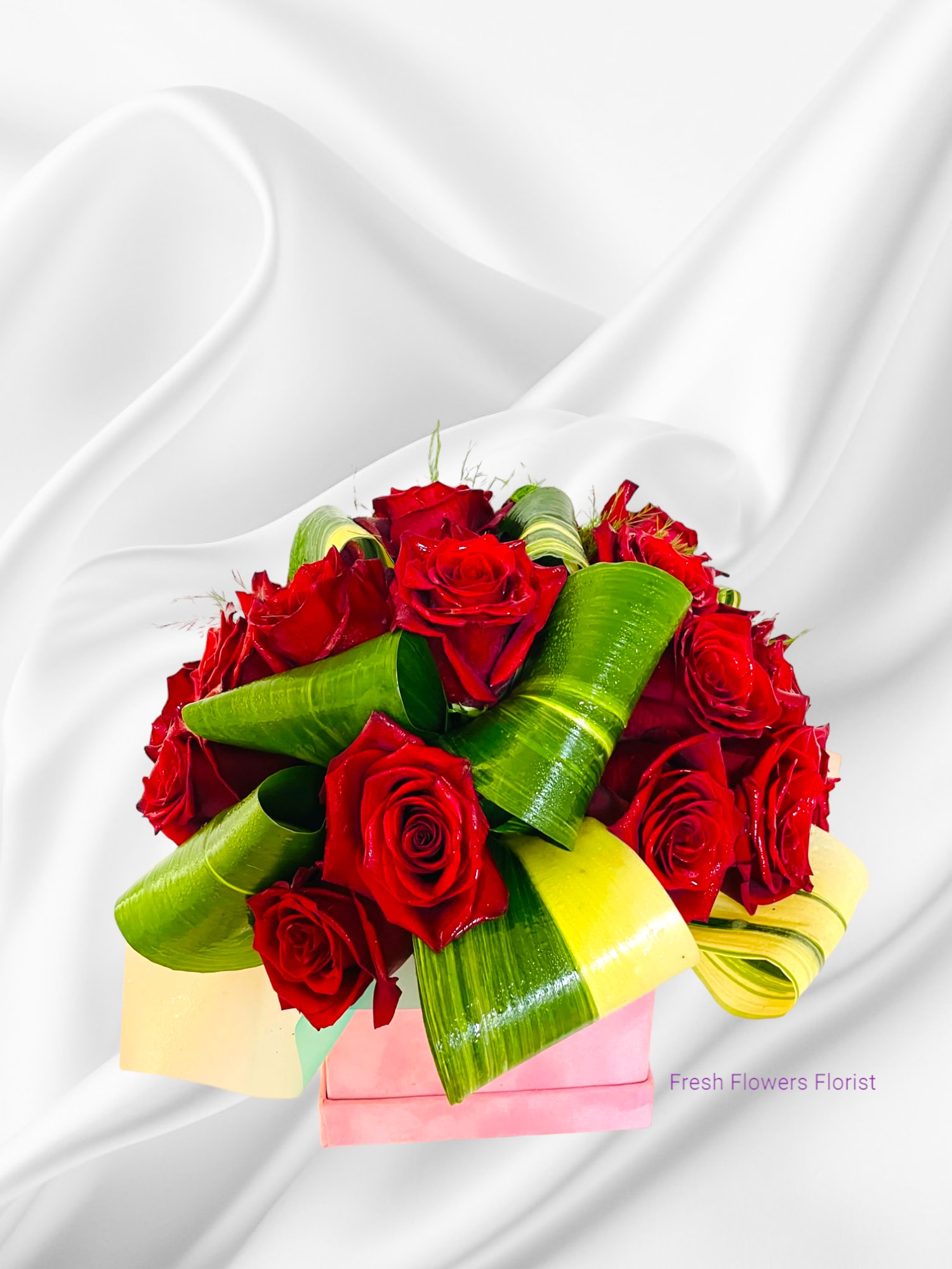 Bouquet of red roses with green and yellow leaf wraps in a pink box