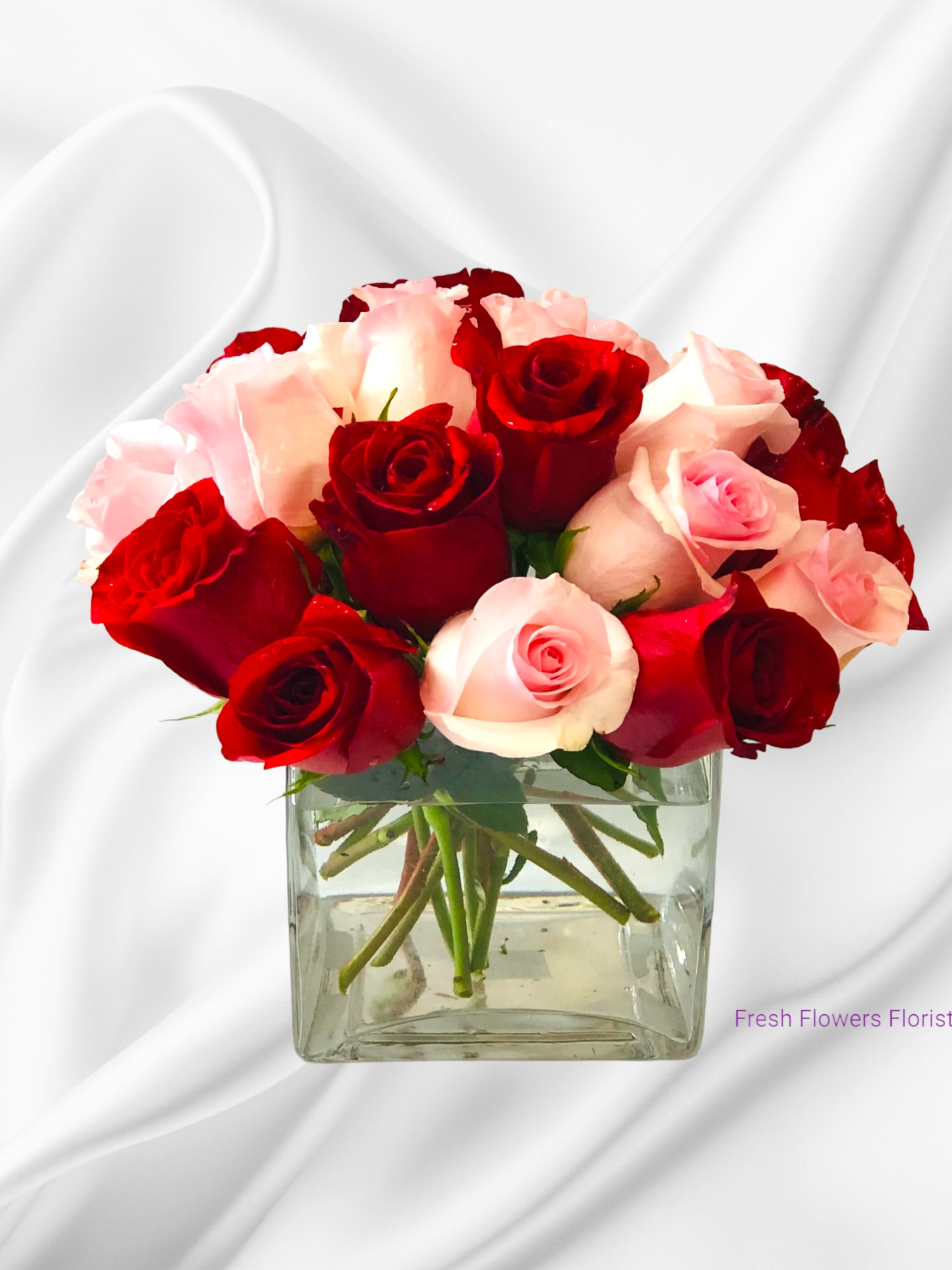 Red and pink roses arranged in a clear square vase