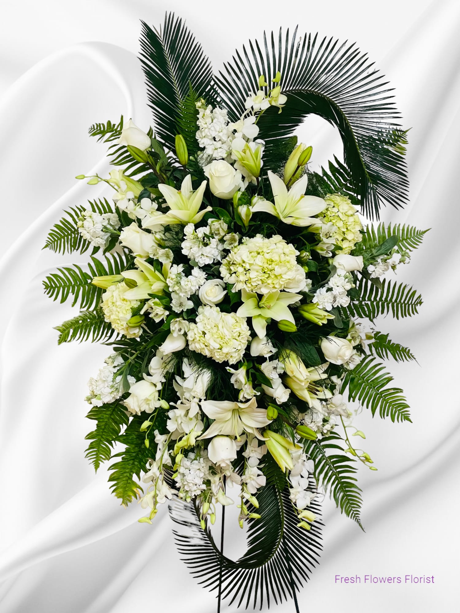 White floral standing spray with lilies and hydrangeas on dark palm fronds