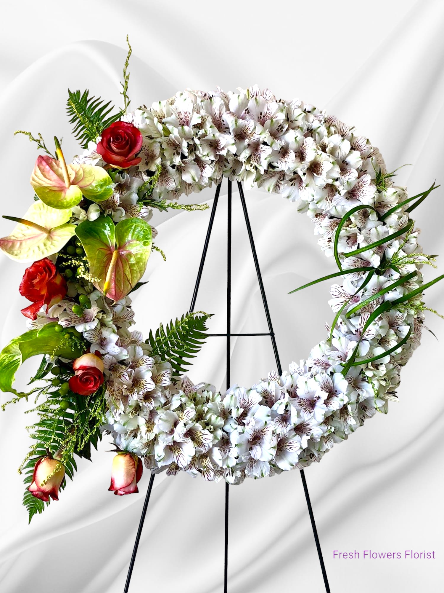 Circular floral wreath on an easel with white blooms and red roses