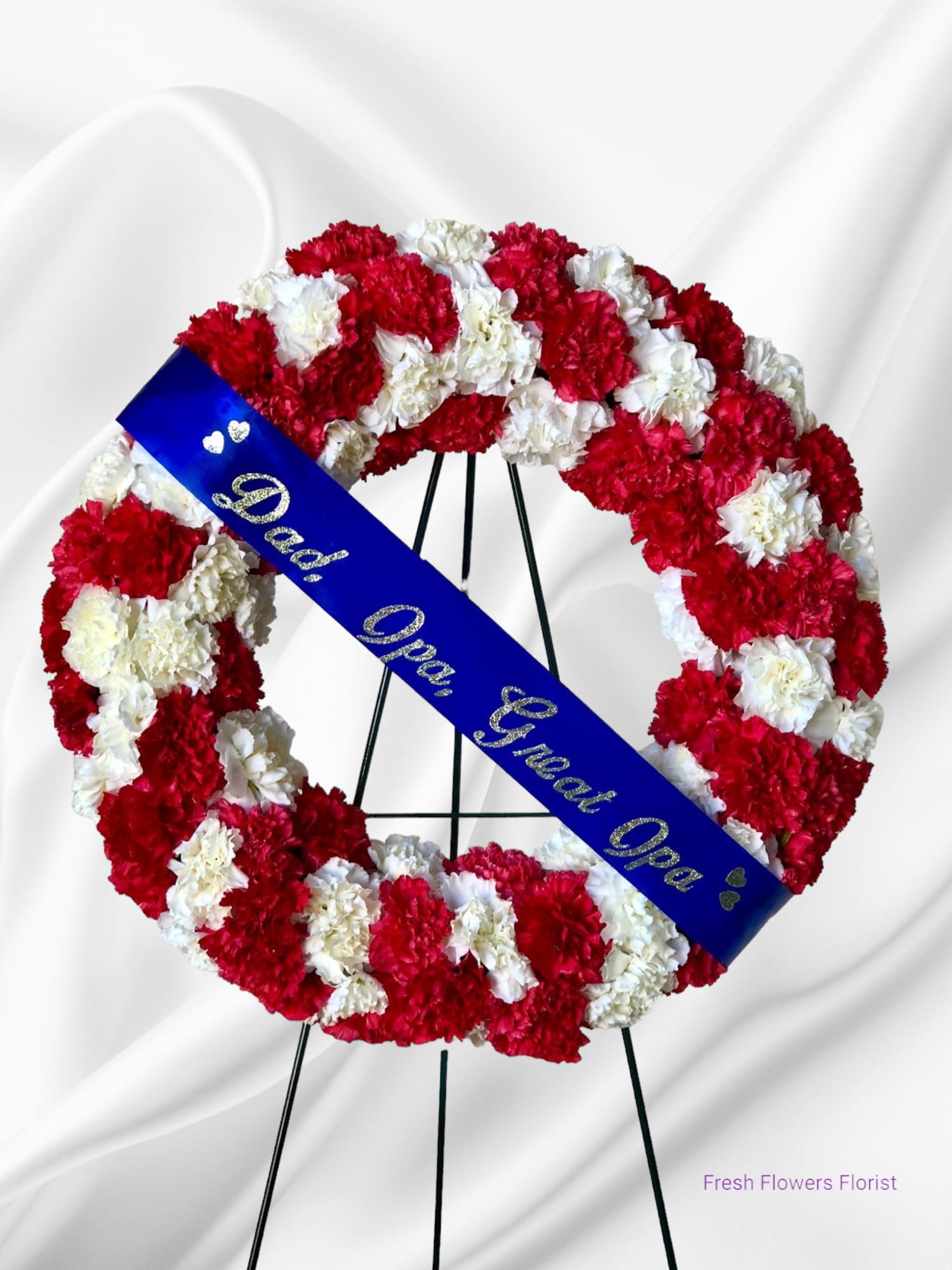 Red and white carnation funeral wreath with a blue memorial sash