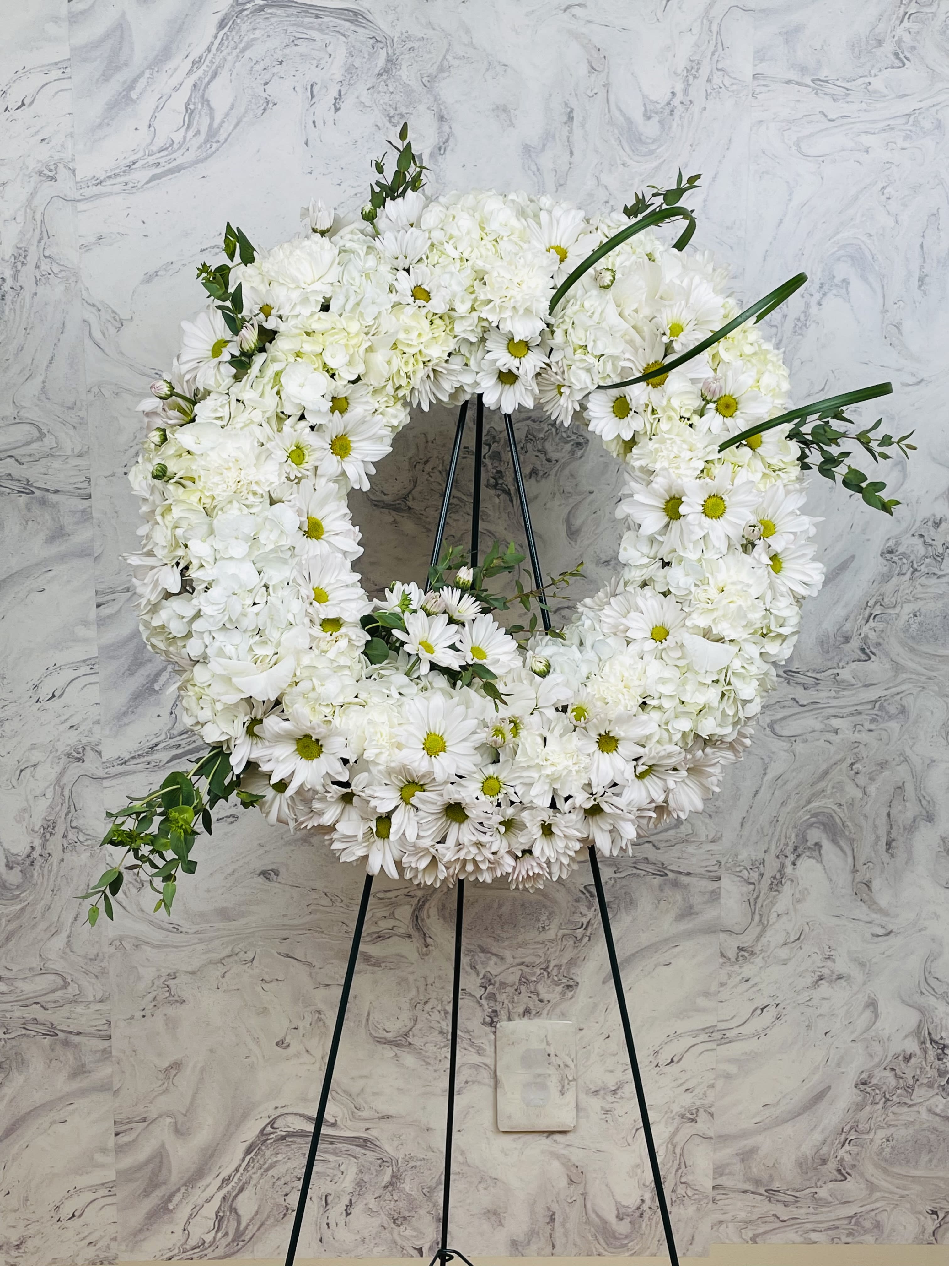 White floral wreath on a black easel with daisies and hydrangeas