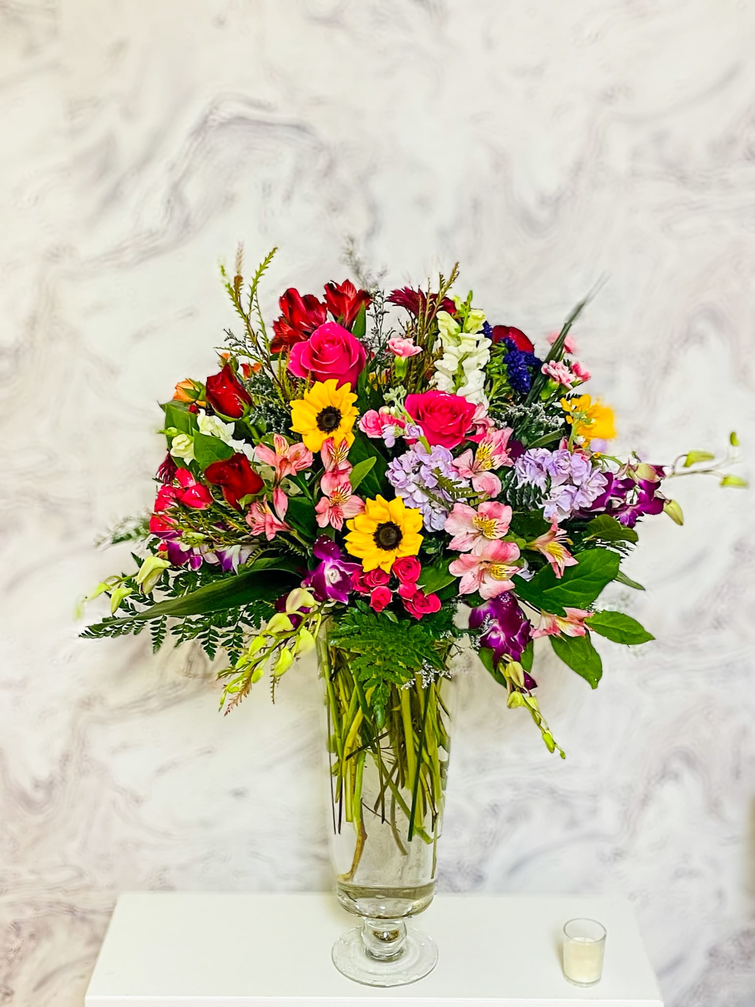 Mixed bouquet of roses, sunflowers, and orchids in a glass vase