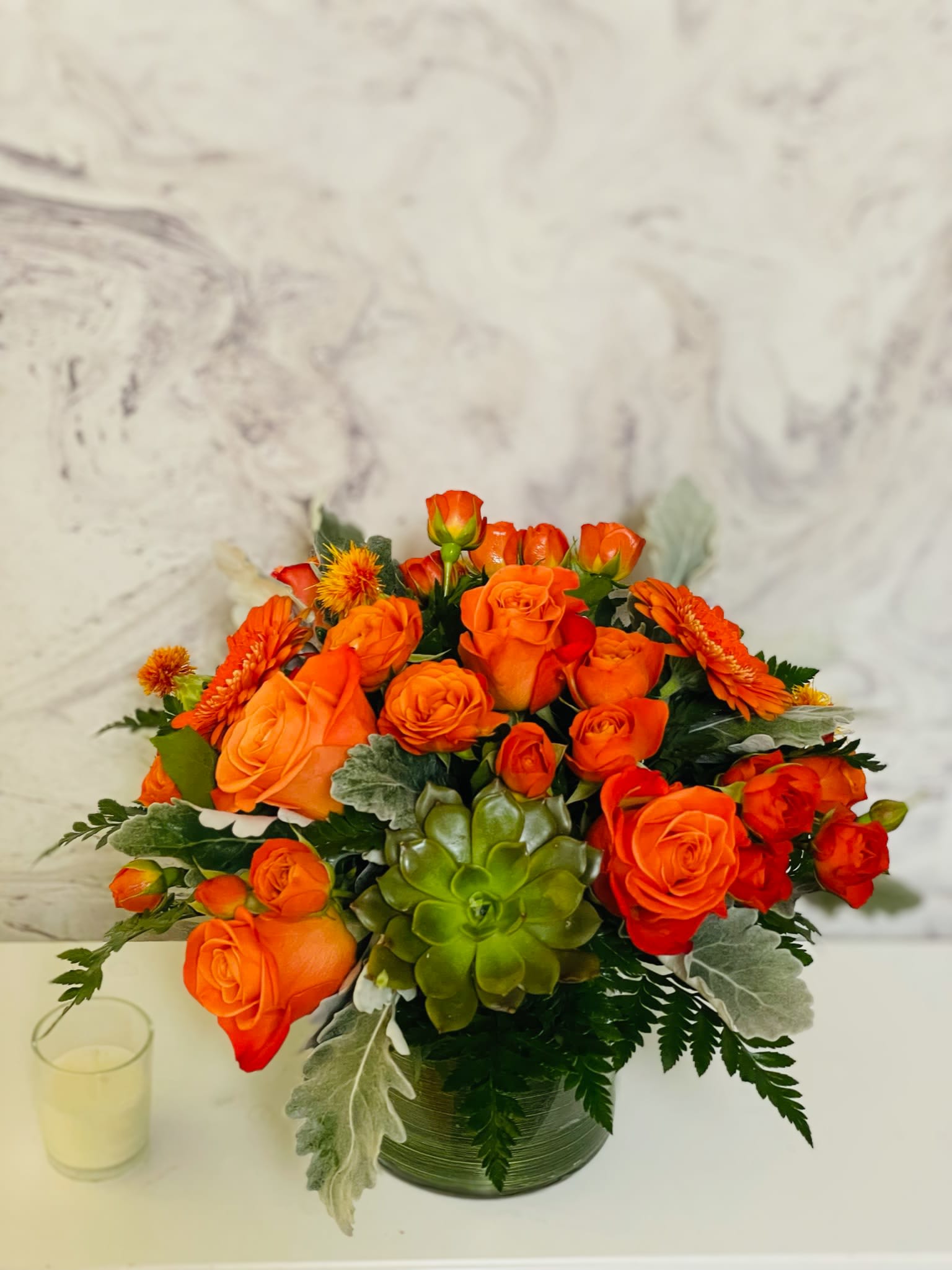 Orange rose arrangement in a glass vase with a green succulent