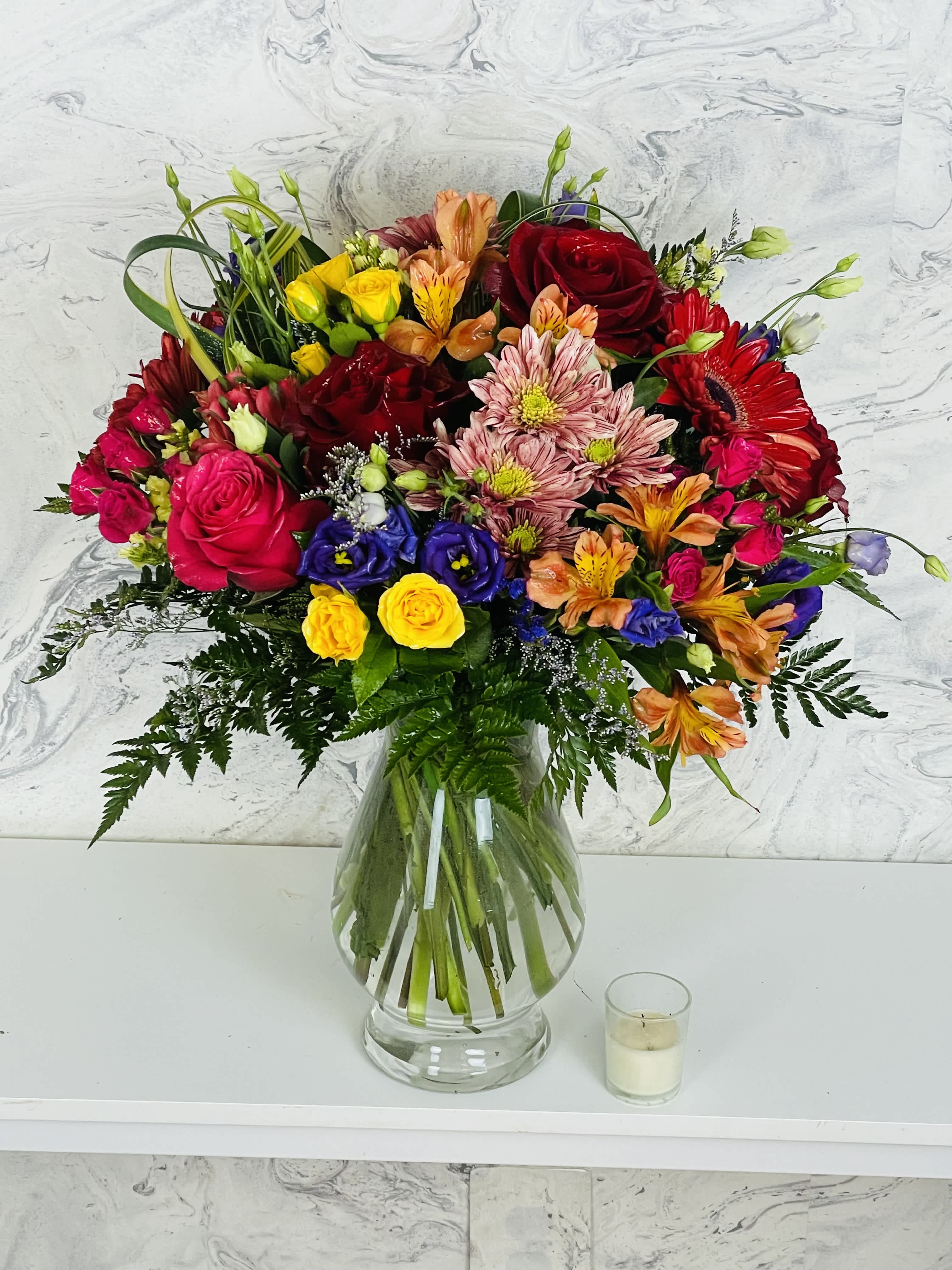 Colorful mixed bouquet in a clear glass vase with roses and daisies
