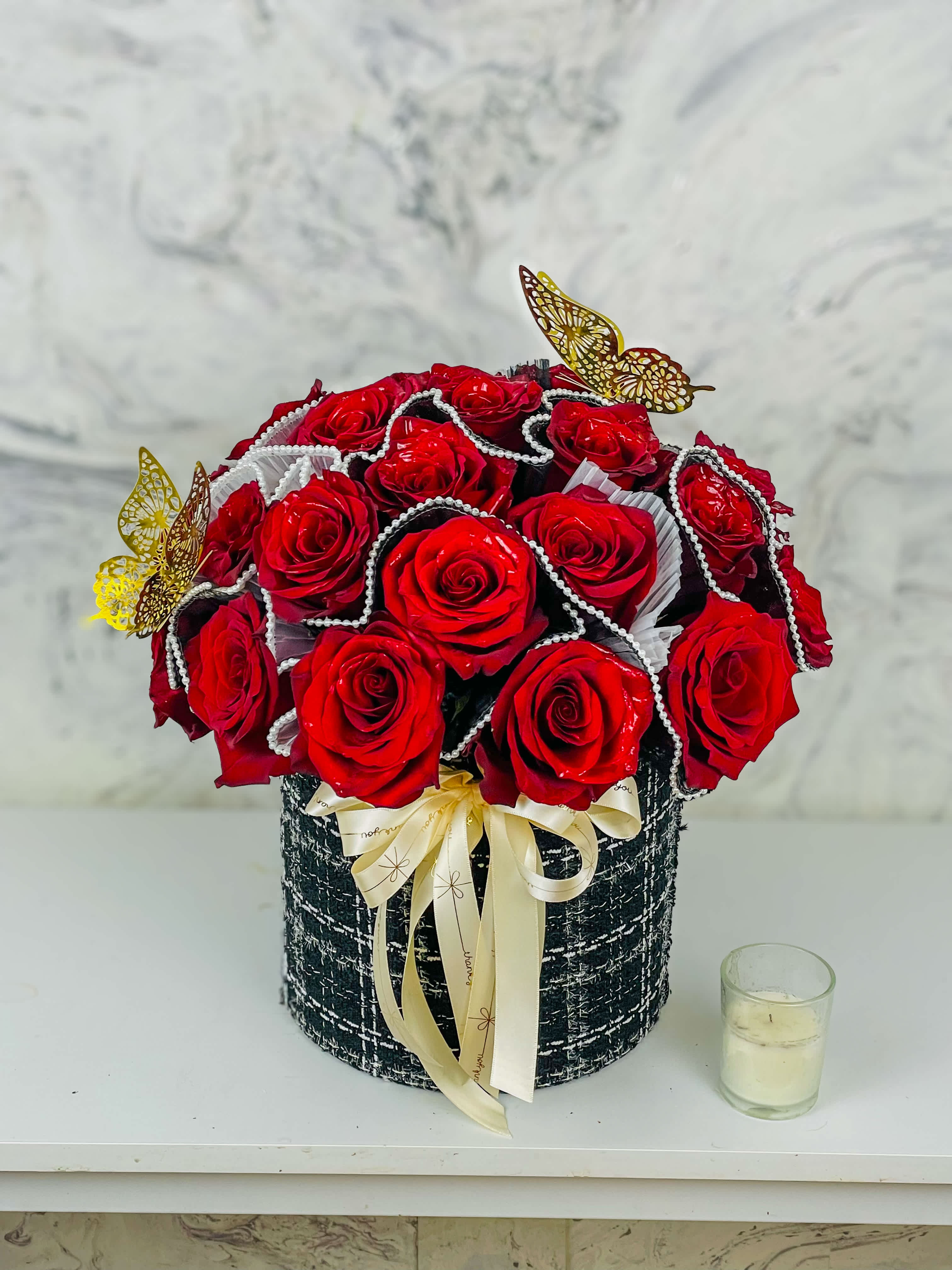 Red roses arranged in a black round box with a cream ribbon