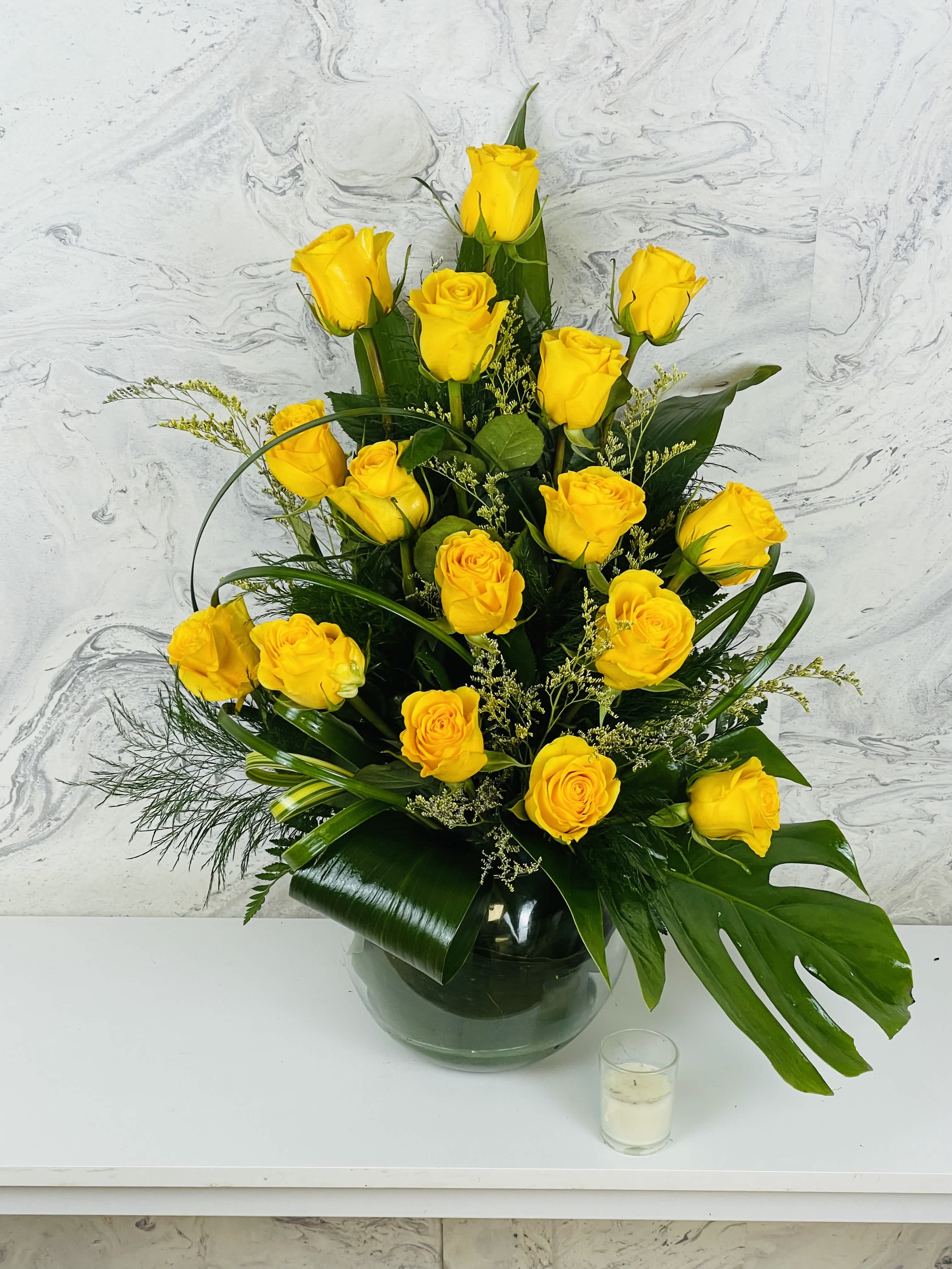 Yellow roses arranged in a glass vase with dark green foliage.