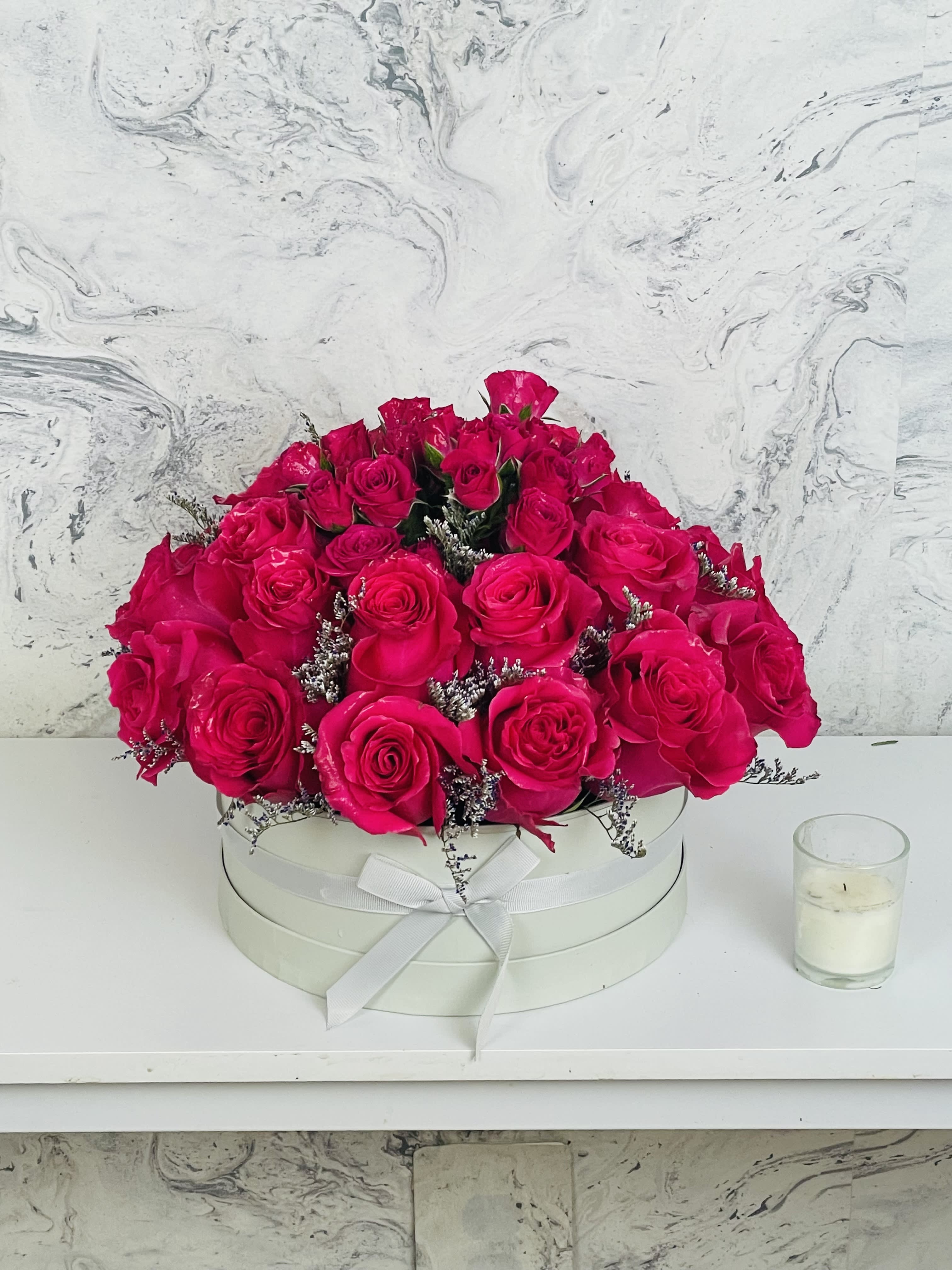 Hot pink roses arranged in a round white box with a ribbon bow