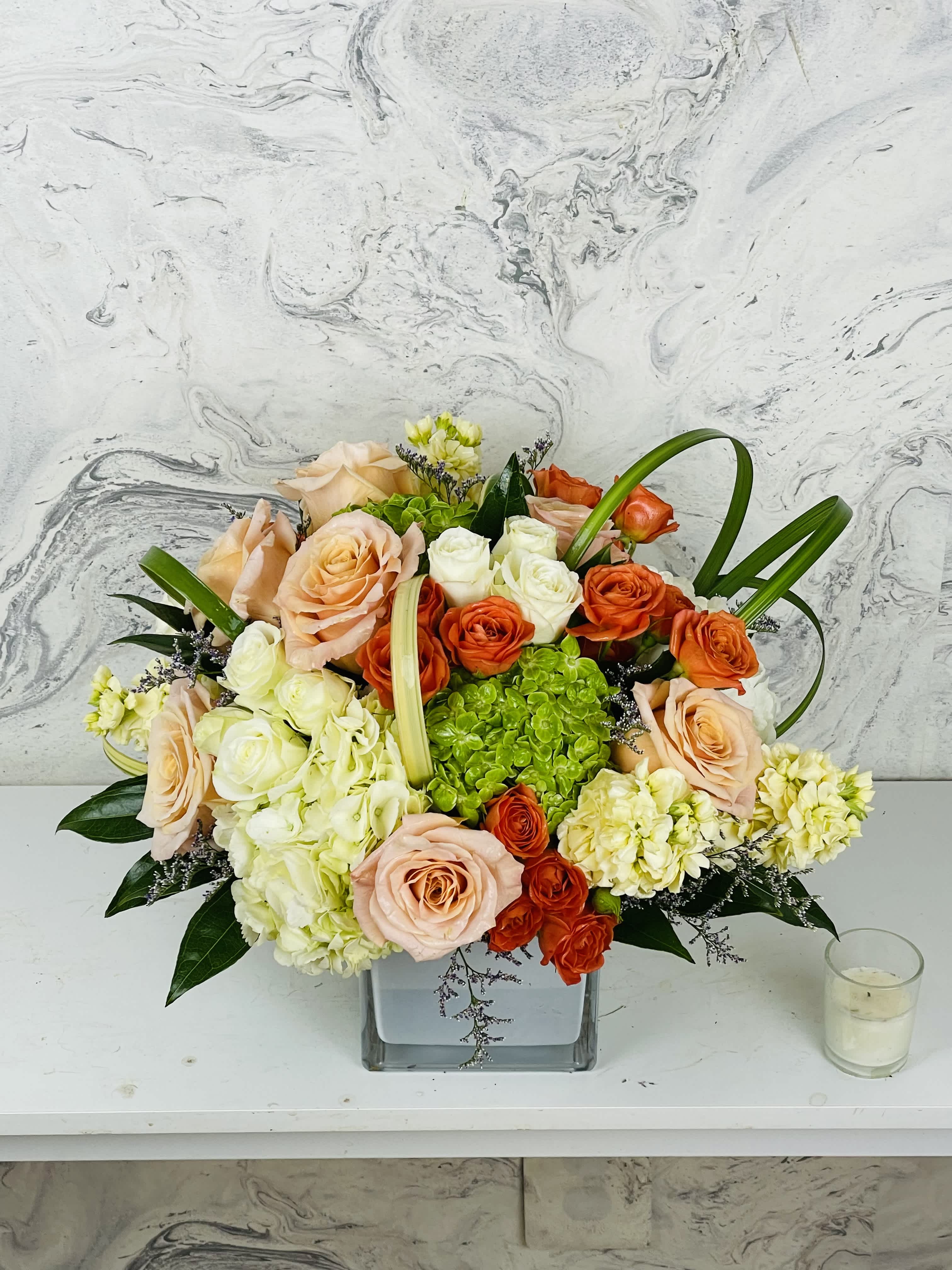 Mixed bouquet of peach, orange, and white roses in a square glass vase