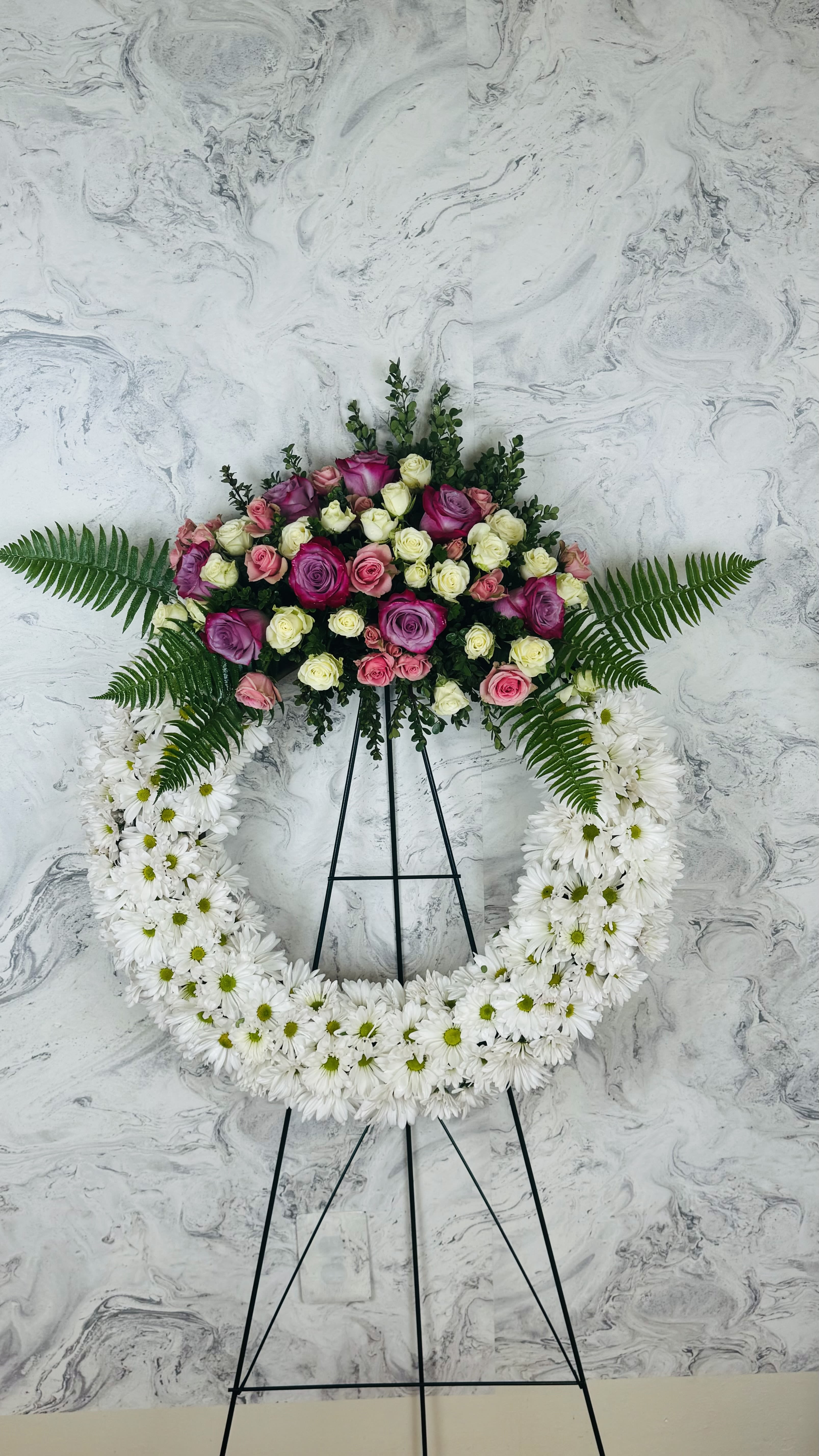 Standing floral wreath with pink and white roses and white daisies on an easel