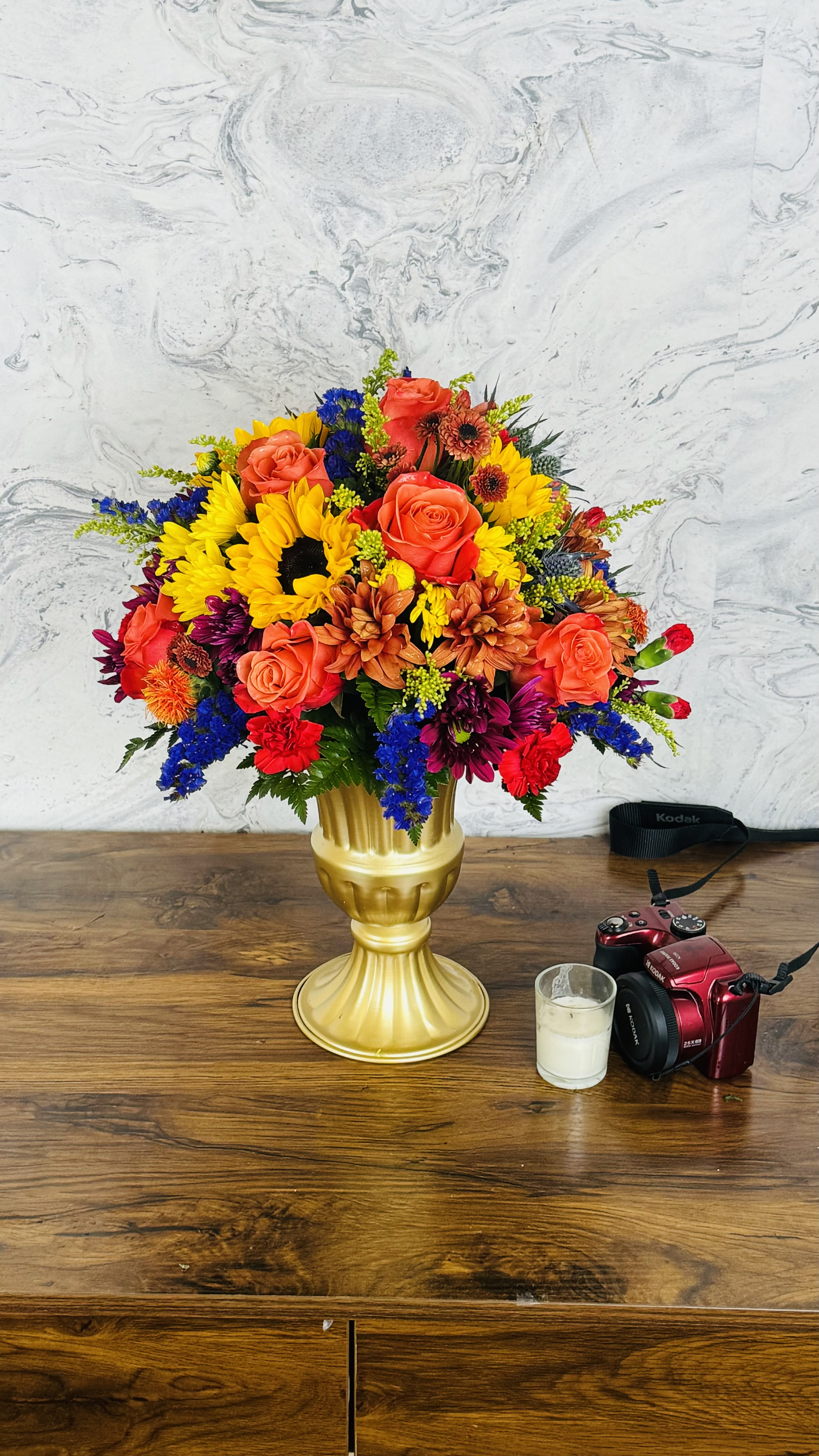 Colorful bouquet of roses, sunflowers, and mixed blooms in a gold vase