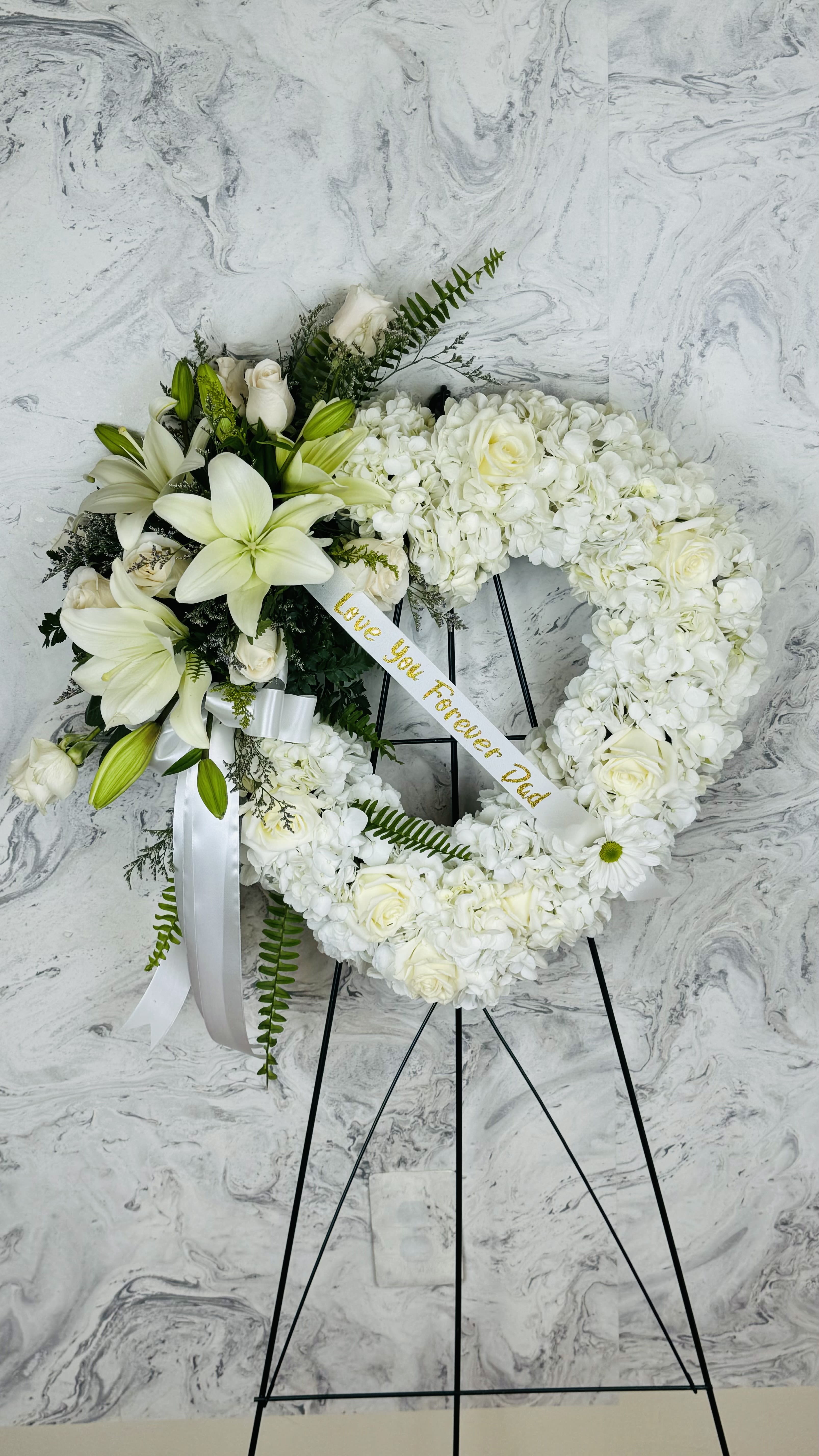 White floral funeral wreath on a black stand with a ribbon