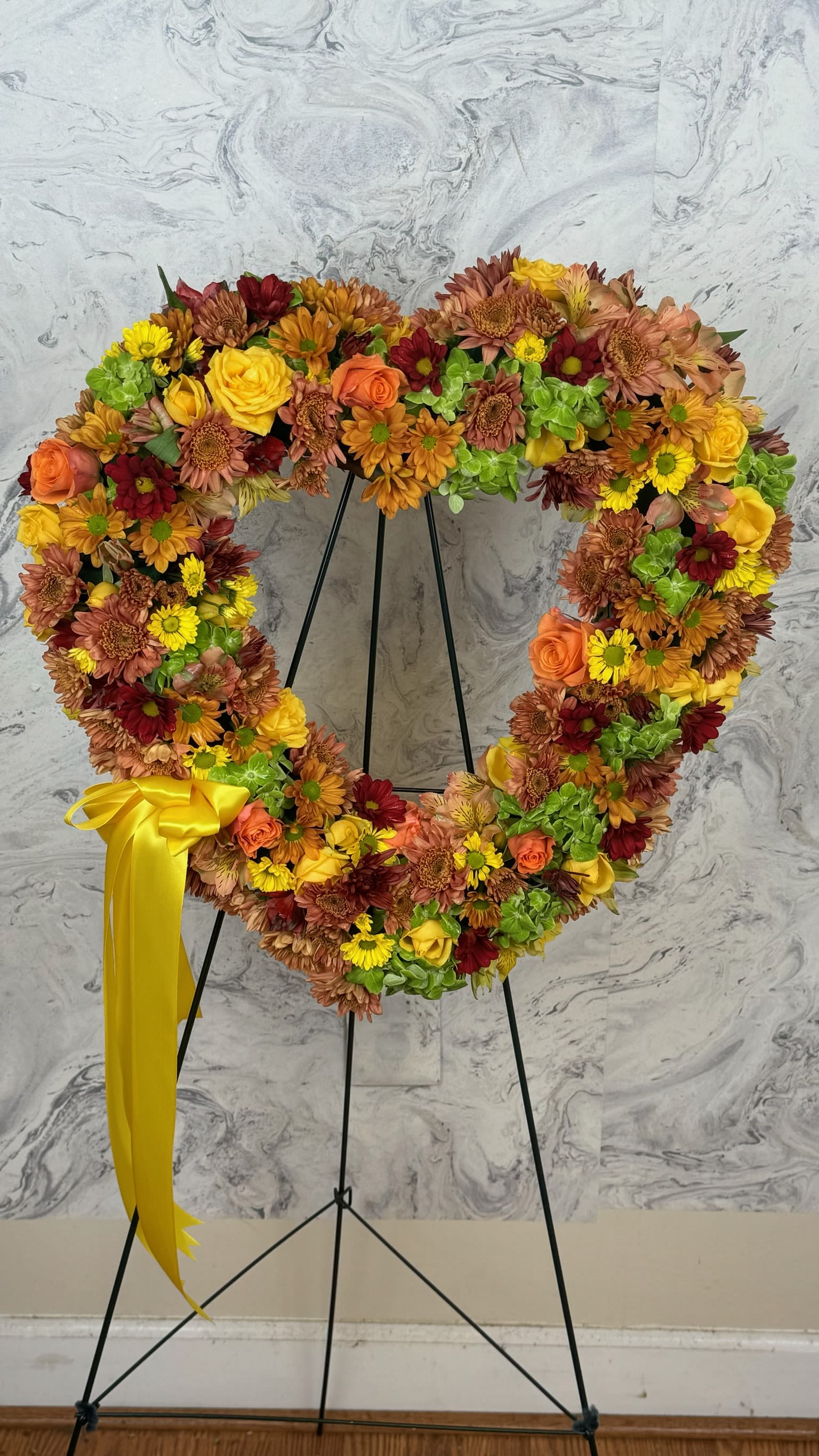Heart-shaped floral wreath on a stand with a yellow ribbon
