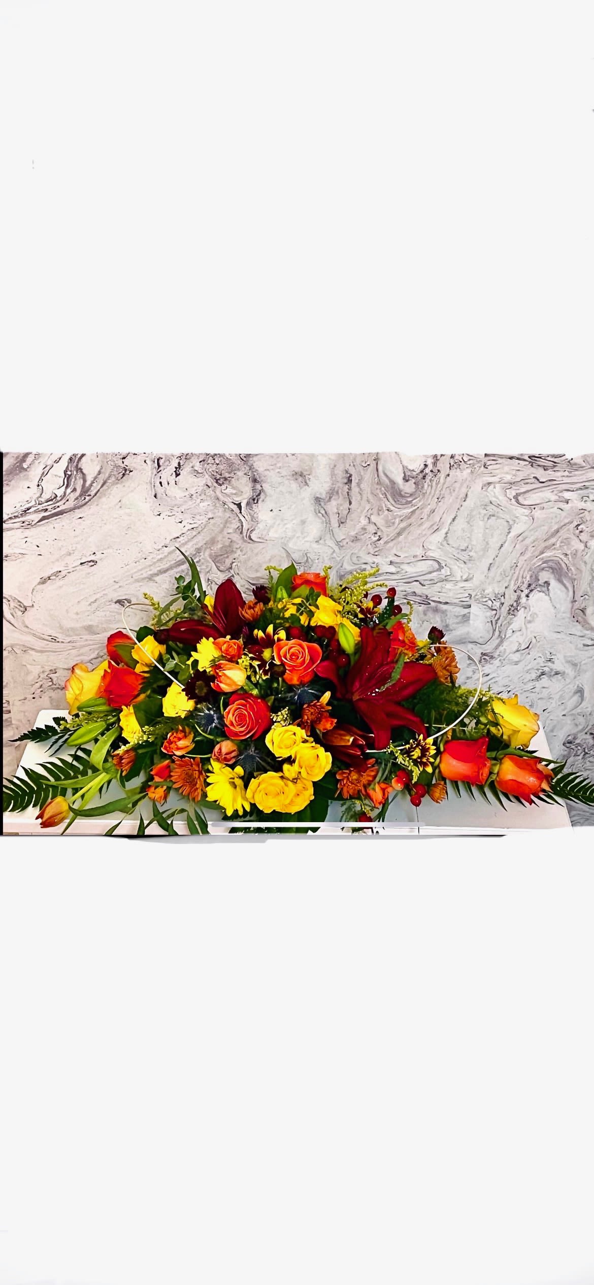 Long low arrangement of red, yellow, and orange flowers on a white base