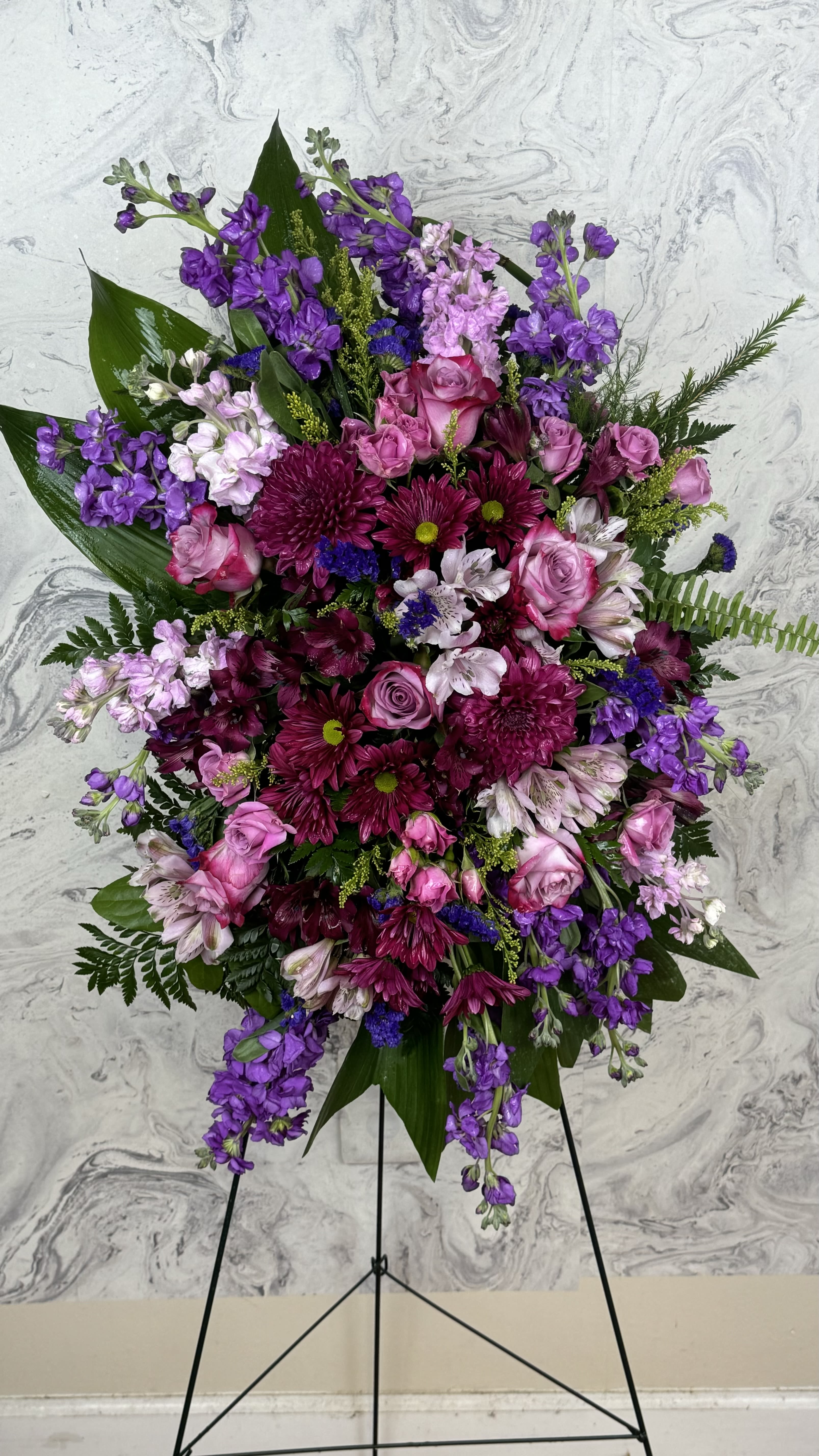 Large standing floral spray with pink and purple flowers on a black easel