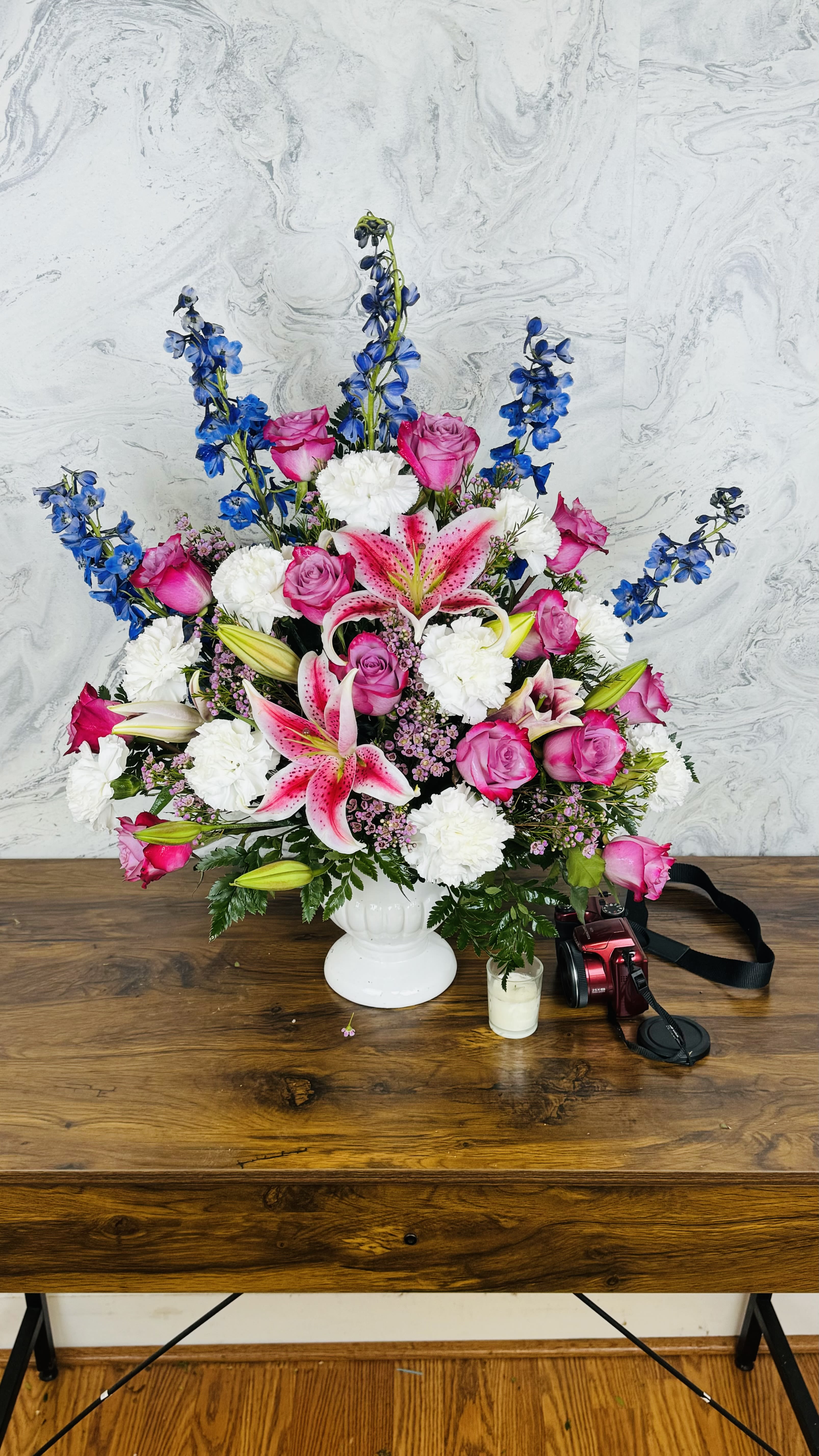 Pink roses and lilies in a white vase with blue delphinium and white carnations