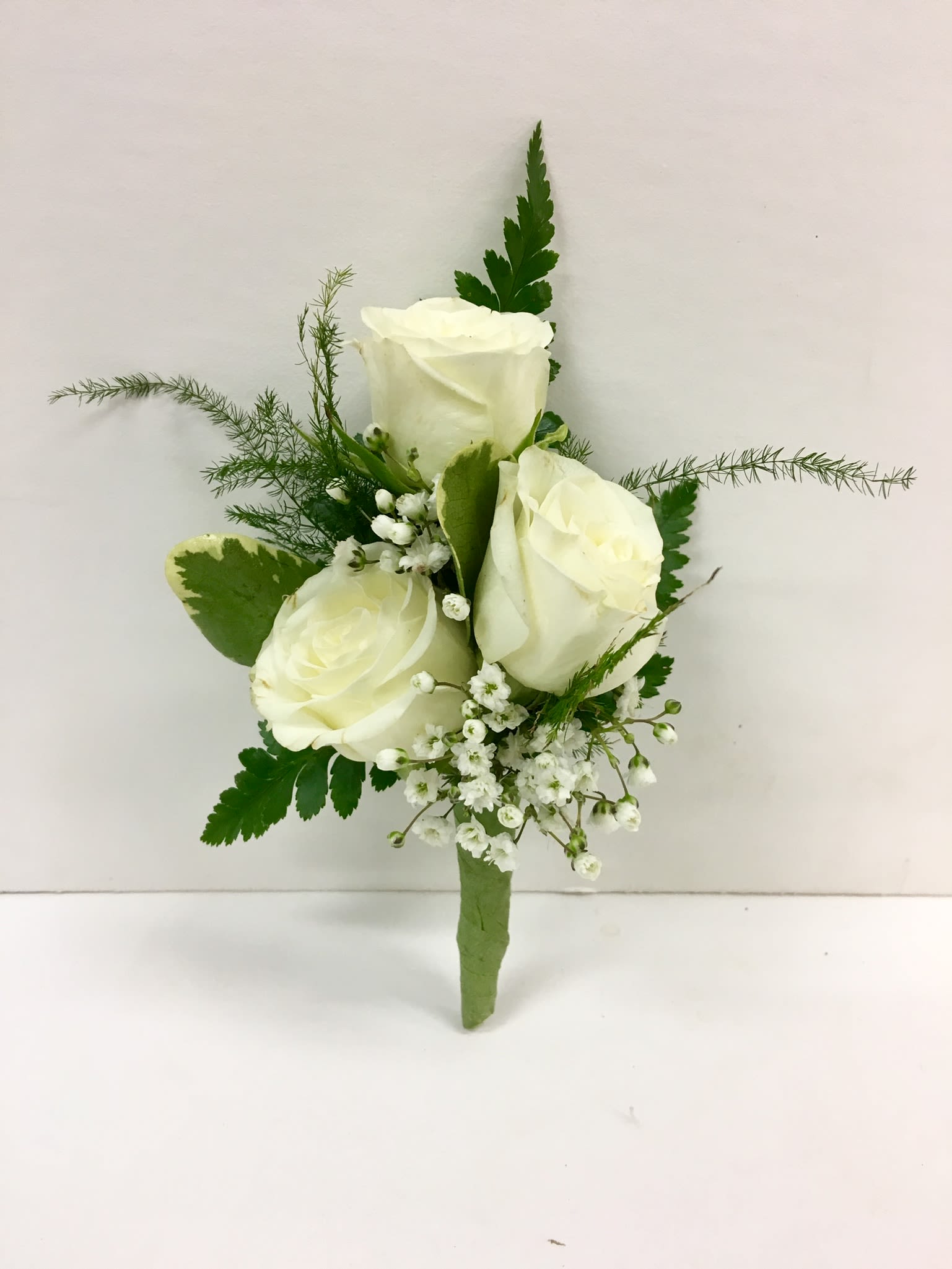 White rose boutonniere with small white filler flowers and greenery