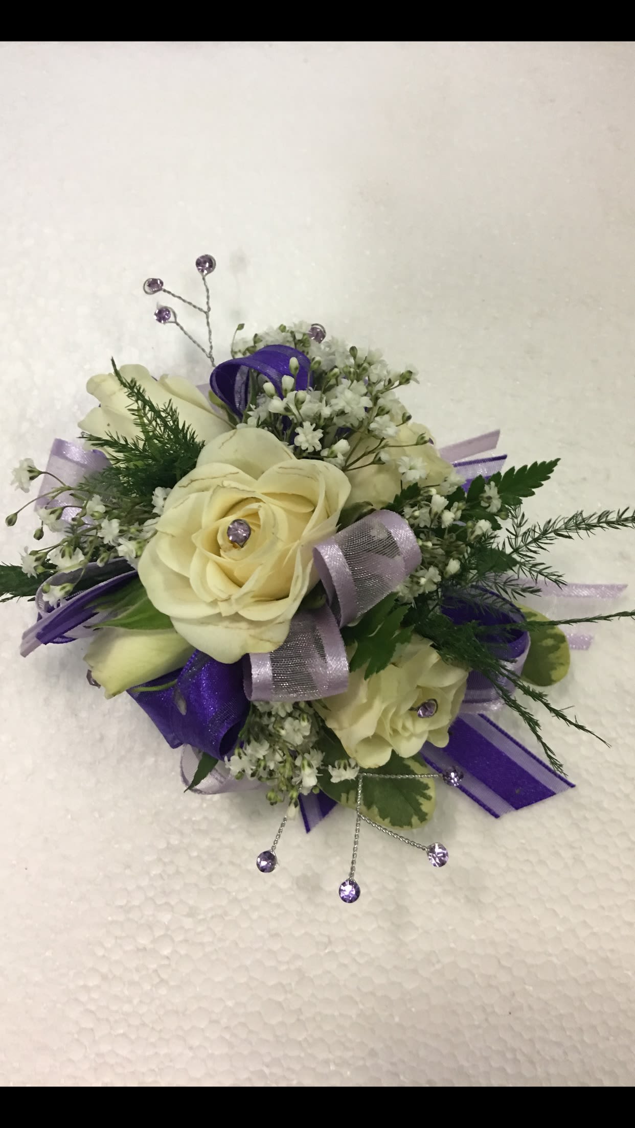 Cream rose corsage with purple ribbon and small white filler flowers