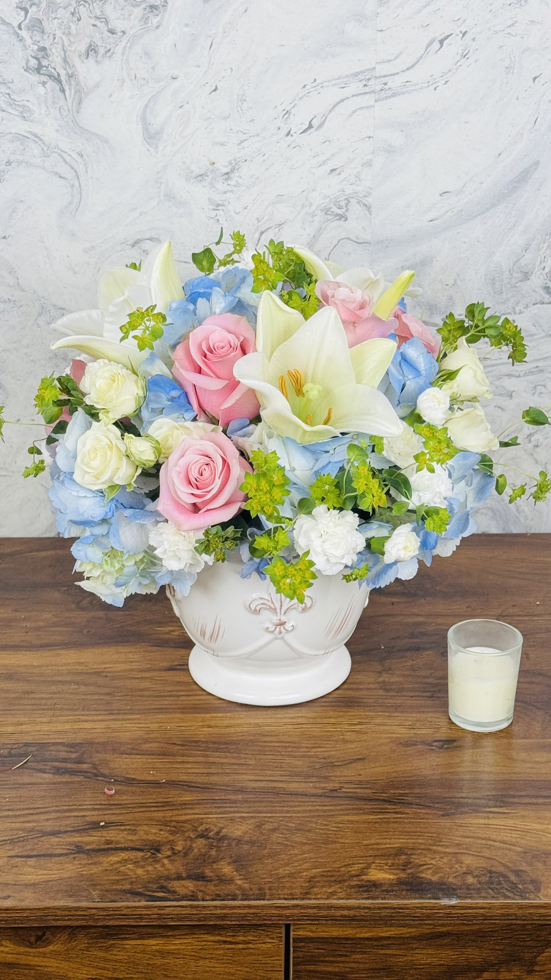 Pink roses and white lilies arranged in a white vase with blue flowers