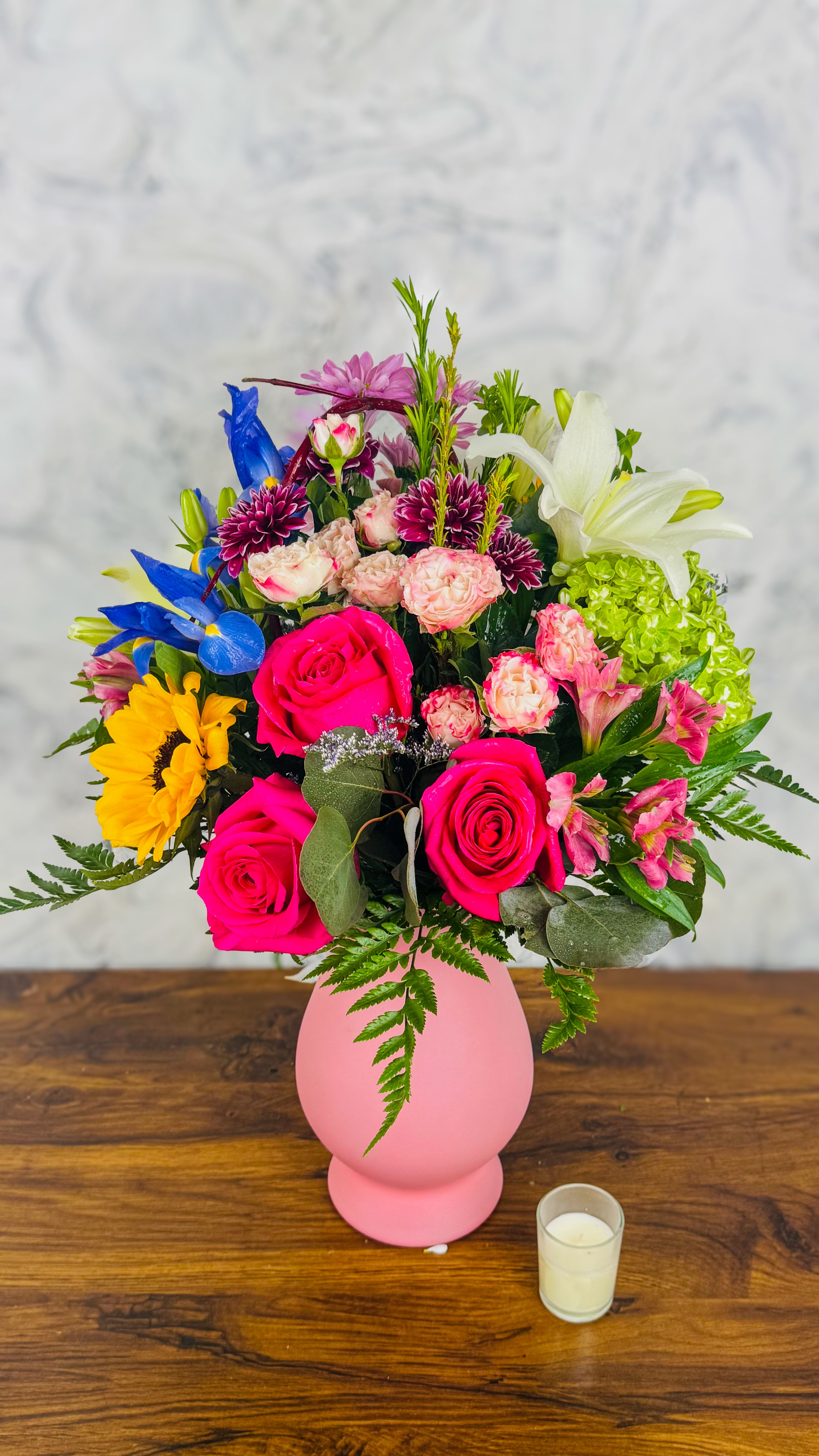Mixed bouquet in a pink vase with roses, lilies, and bright accent flowers