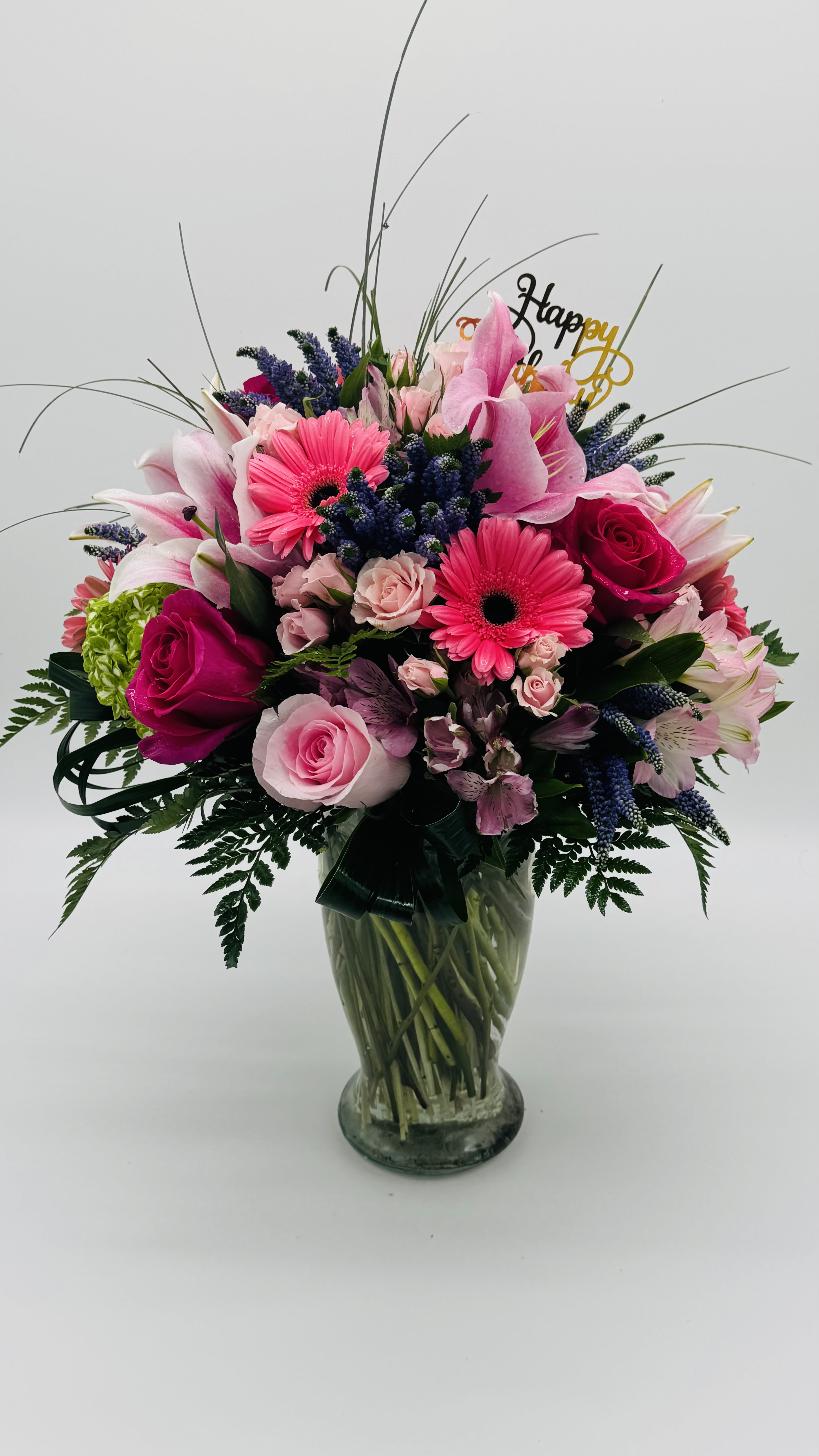 Mixed pink and purple bouquet in a glass vase with a Happy Birthday topper