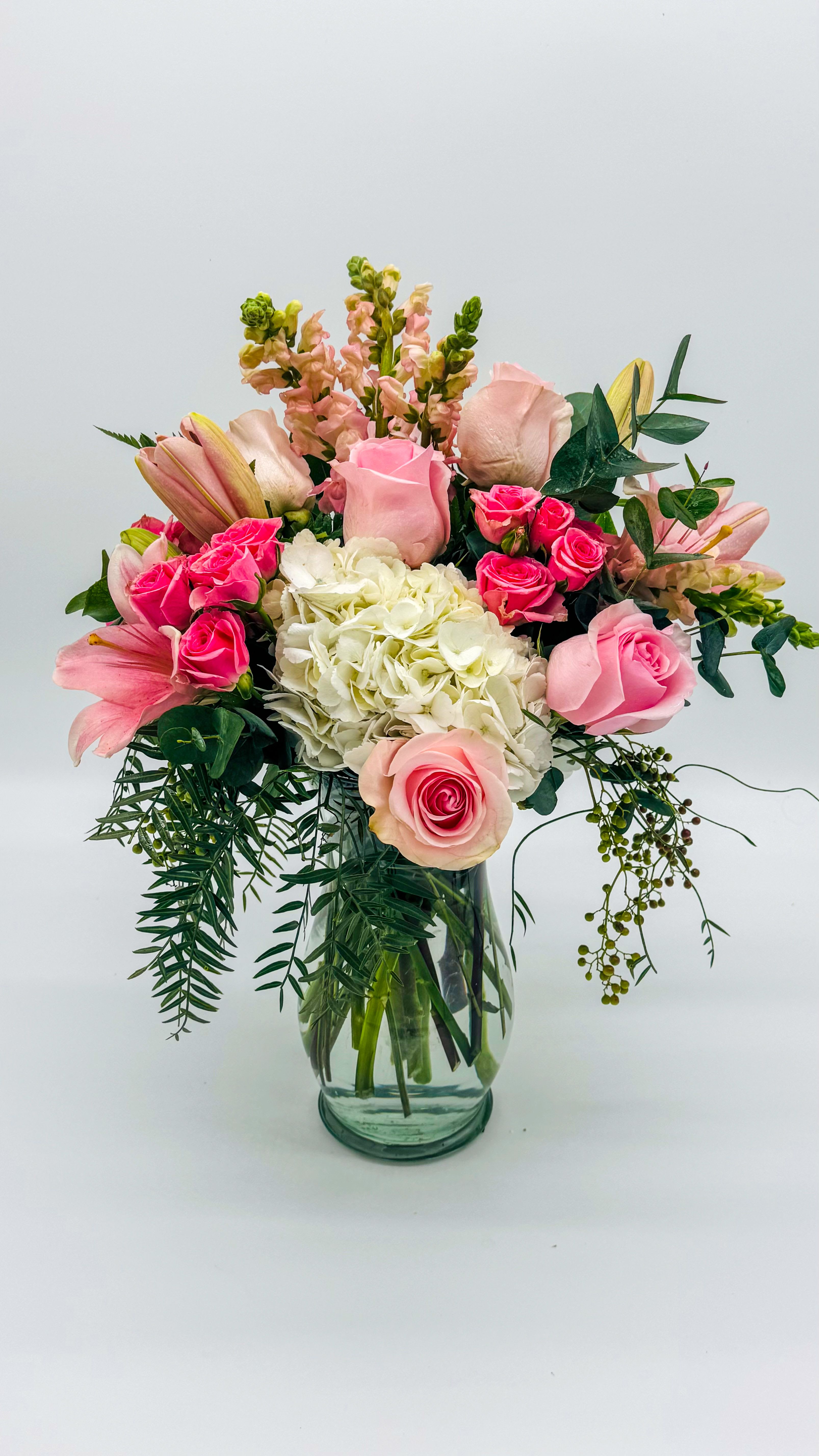 Pink roses and lilies arranged in a glass vase with white hydrangea