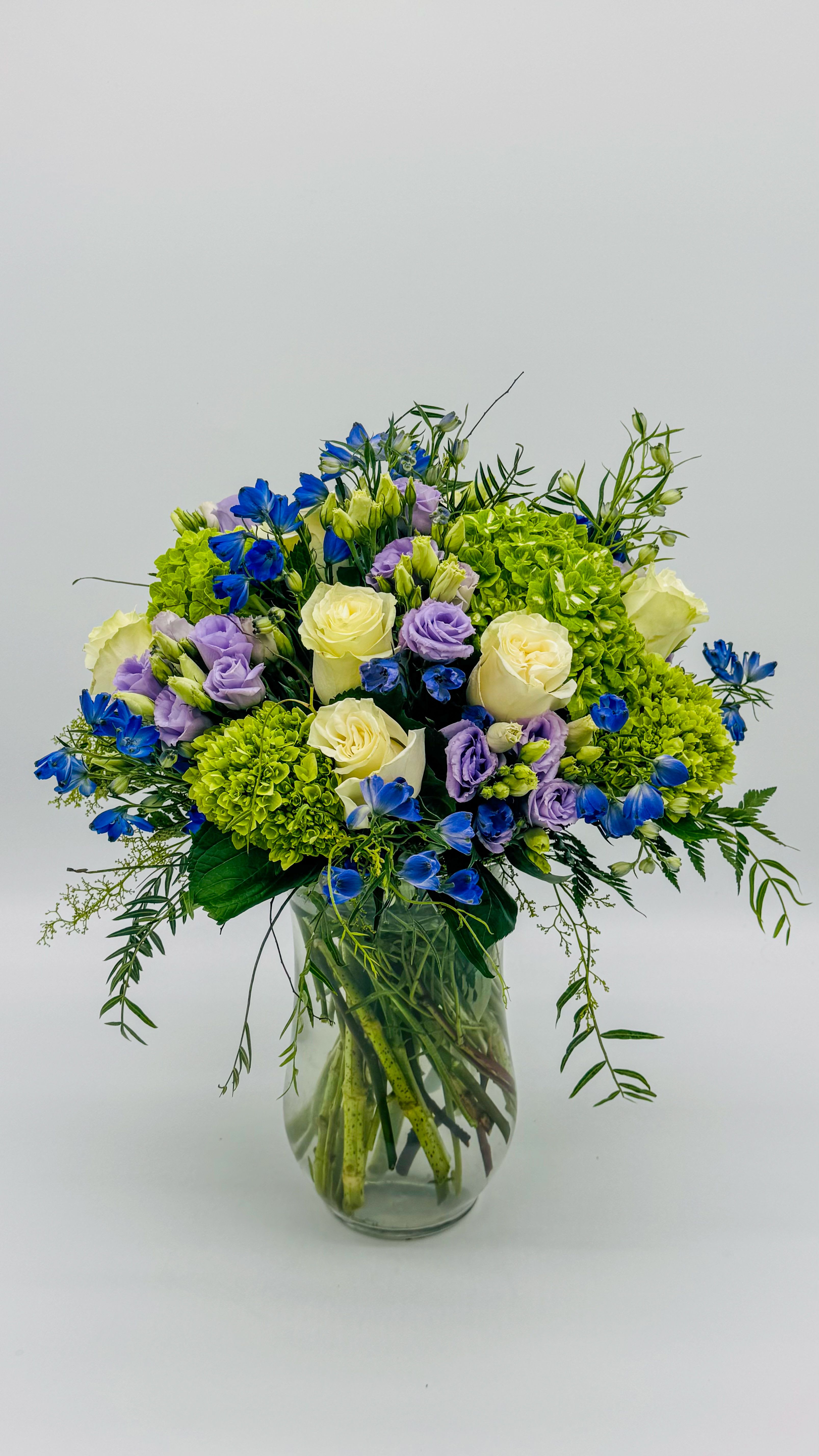 Bouquet of blue, lavender, and white flowers in a clear glass vase